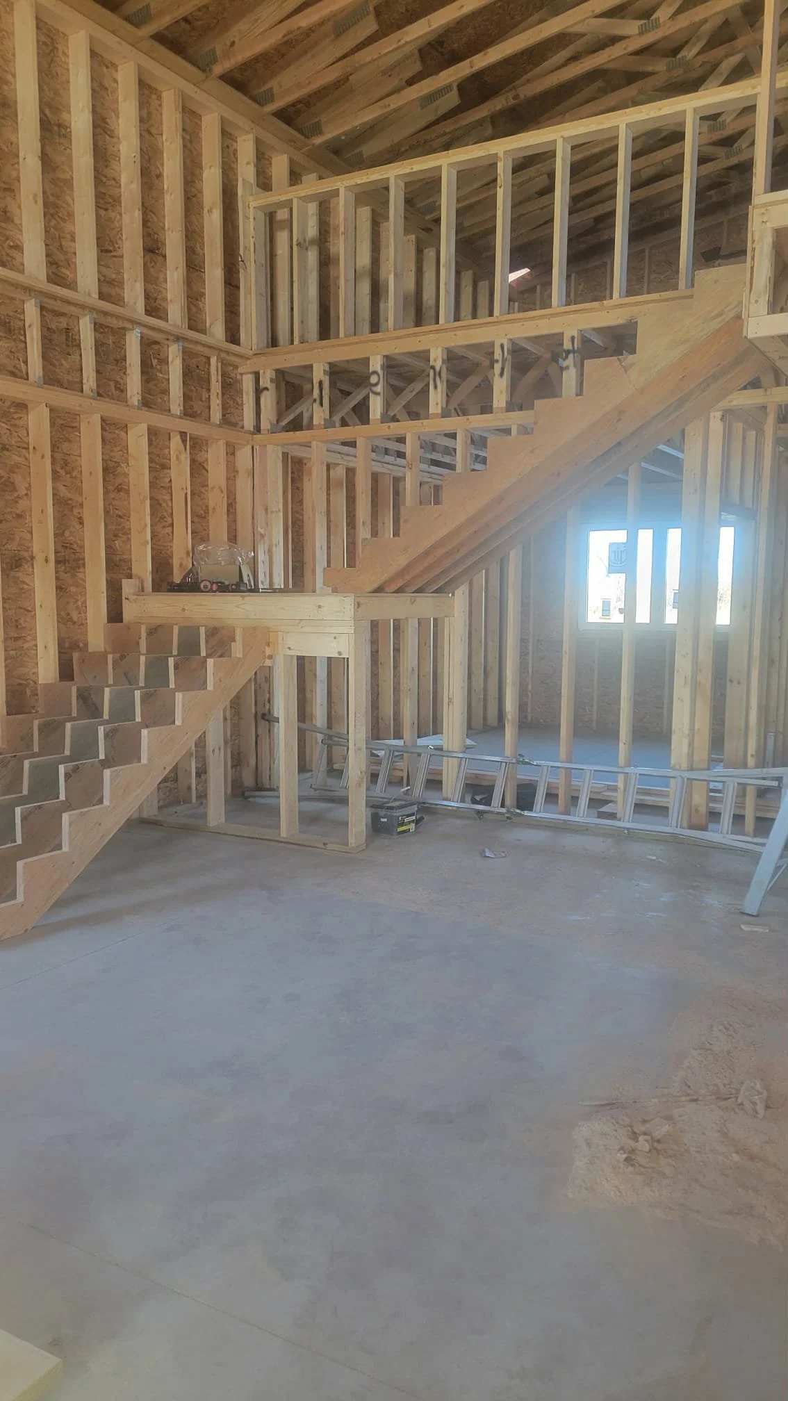 Interior view of a house under construction with exposed wooden framing and stairs.