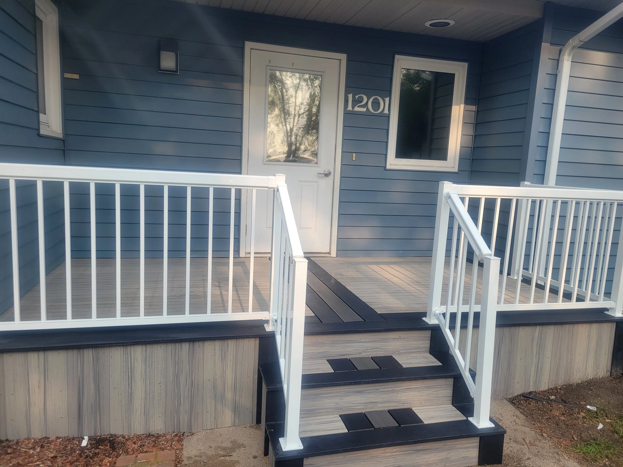 Front porch with white railing, wooden steps, and a blue house with a door and window.