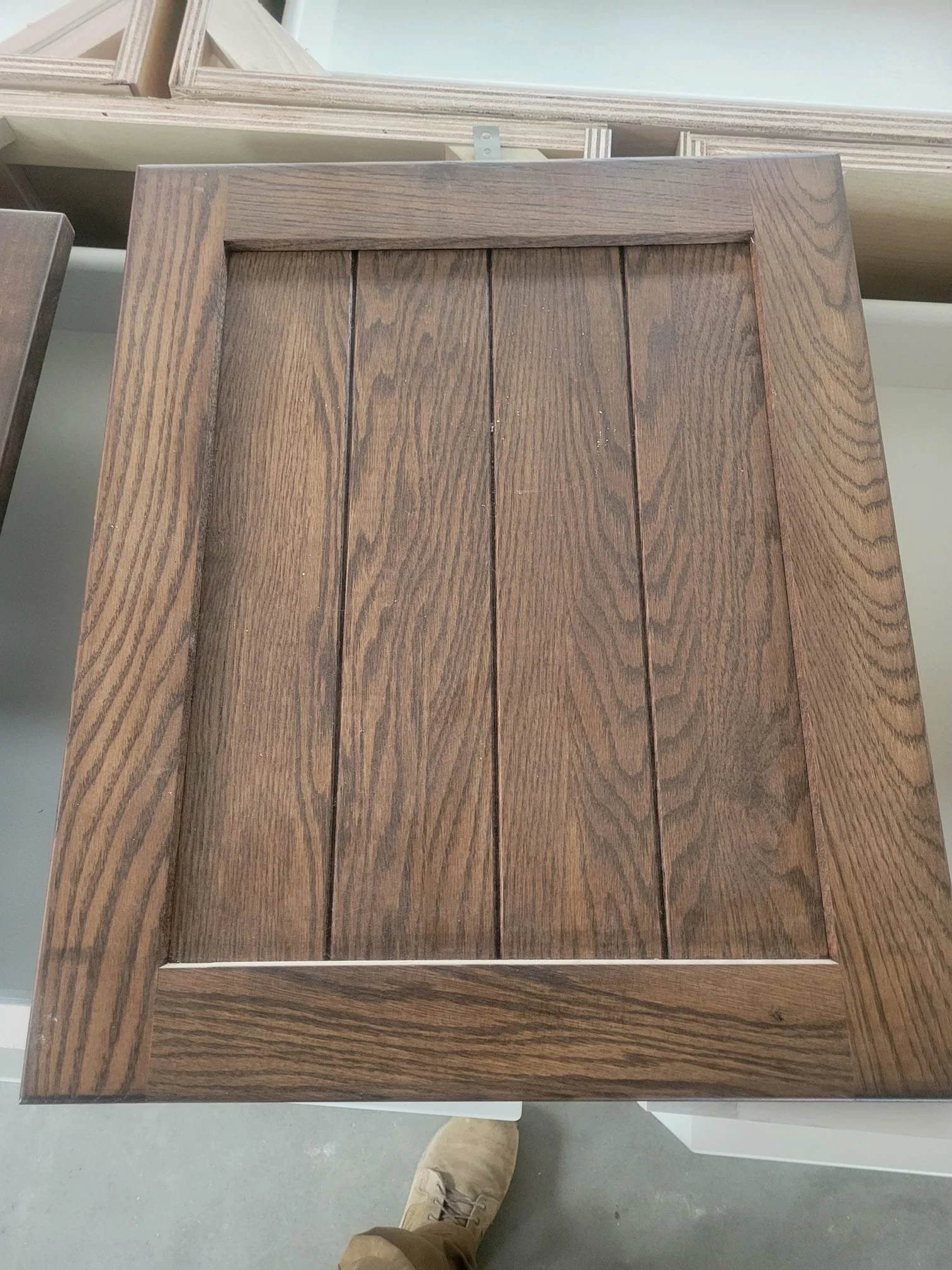 Close-up of a wooden cabinet or door with a natural finish, showing the wood grain pattern with three vertical panels and a frame around them.