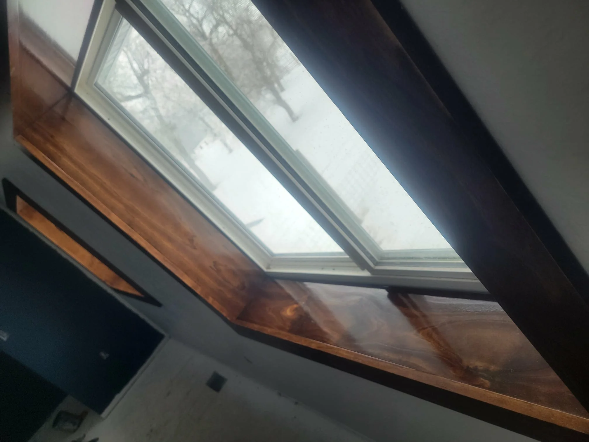 A close-up view of a window with a wooden frame, showing an outside snowy landscape with trees and a fence, seen from inside a room.