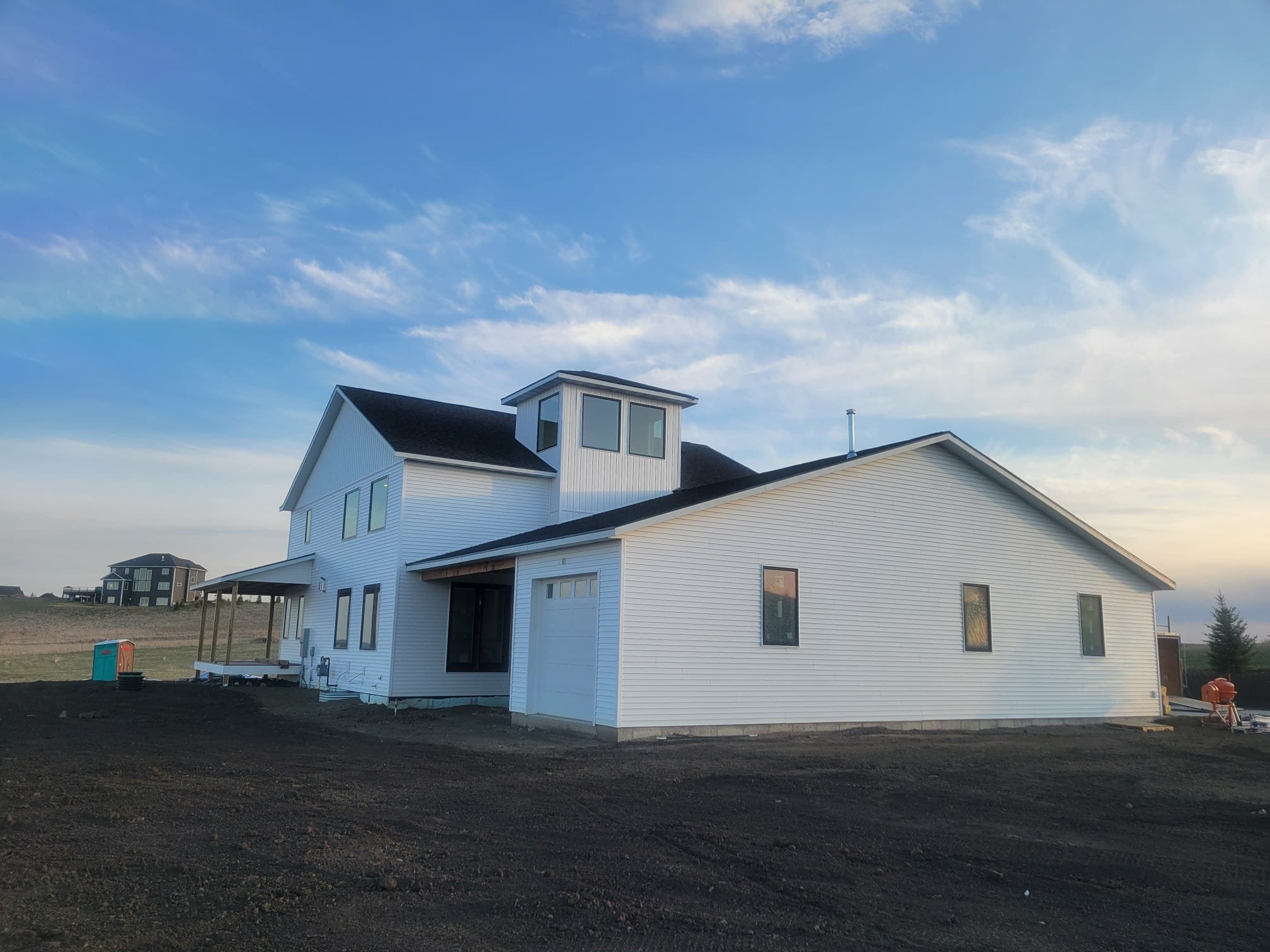 New white house under construction on a dirt lot, with a partly cloudy sky in the background.
