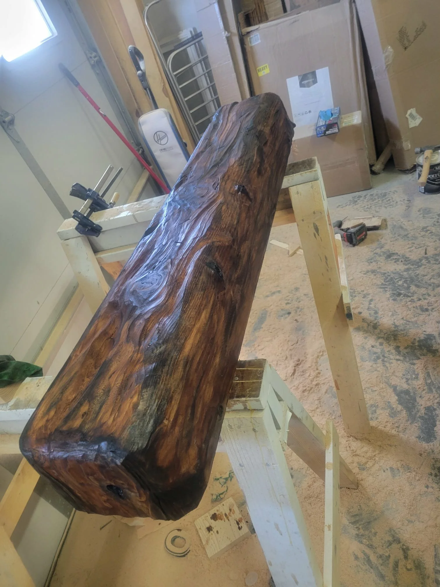 A large, polished, dark wooden log mounted on a workbench in a woodworking shop.  Custom carved mantle