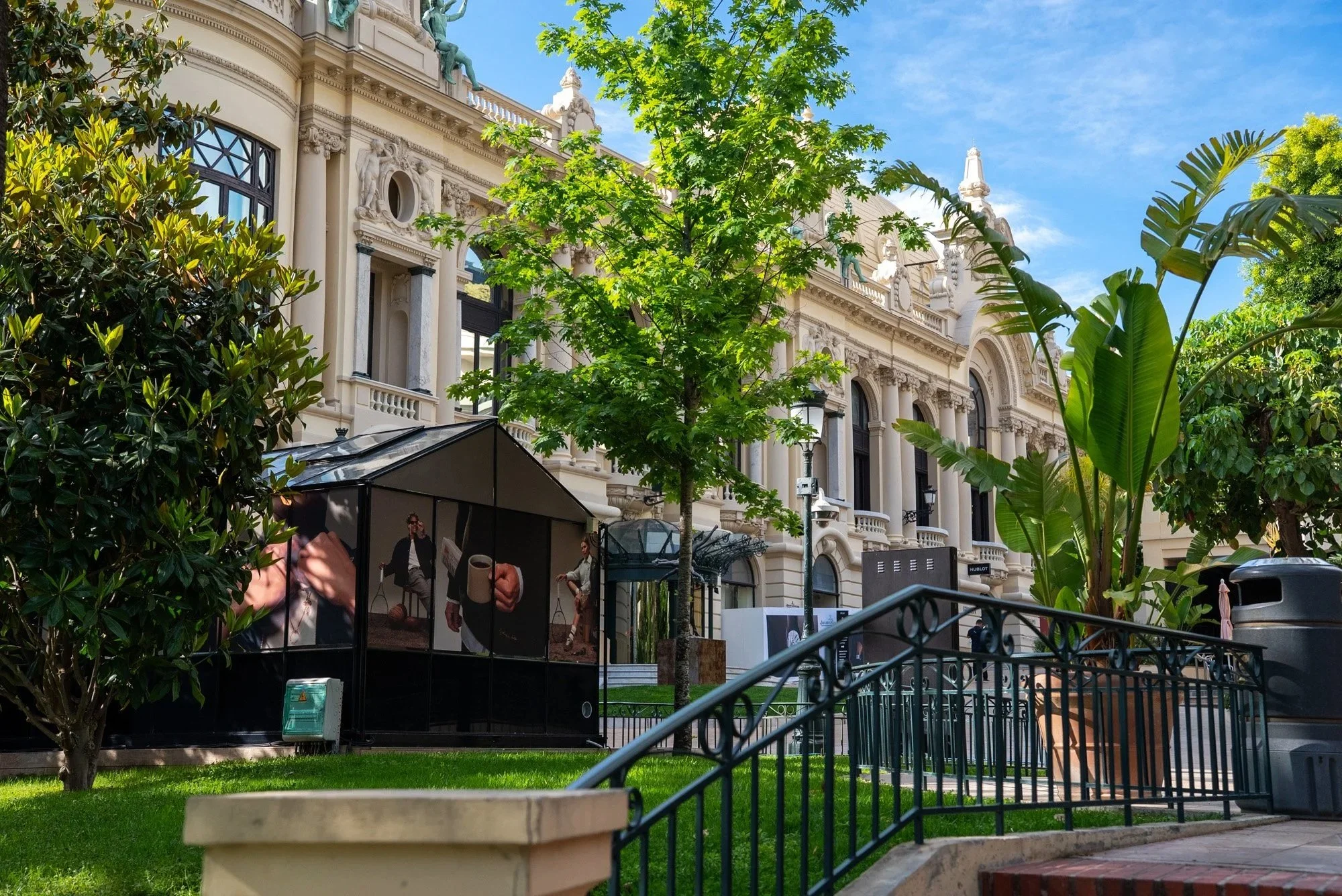 A large ornate building with detailed sculptures and decorative elements on its cream-colored facade, surrounded by green trees and plants, under a blue sky. Event Photography in Monaco for Passaporta.eu