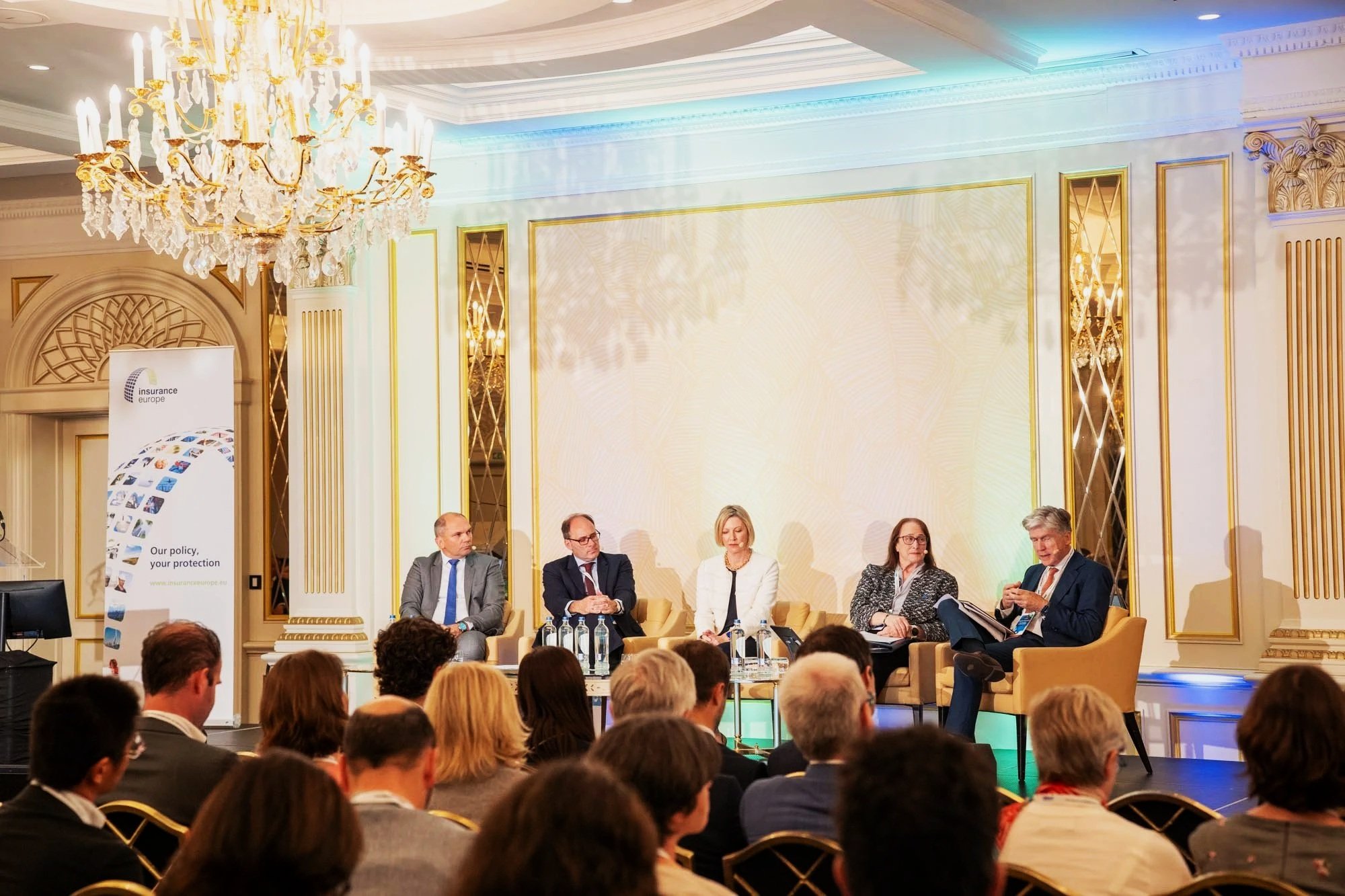 A group of five people sitting on a stage at a conference or panel discussion, with an audience visible in the foreground.Insurance Europe’s 16th International Conference at the Steigenberger Icon Wiltcher’s Hotel, Brussels.