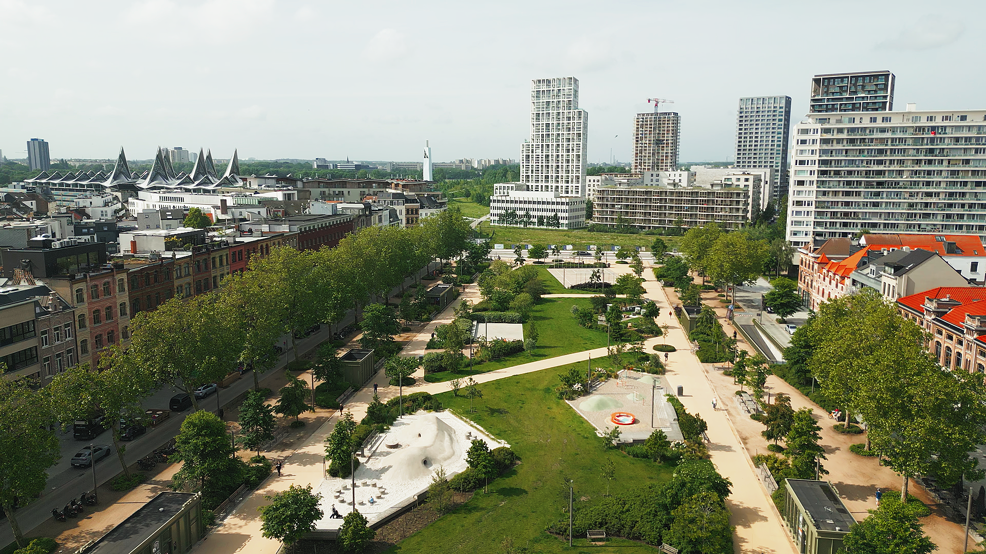 A city park with pathways, trees, and playgrounds, surrounded by modern high-rise buildings and residential houses. johnson & Johnoson Finance day 2026 at Tv studio Play Antwerp Zuid