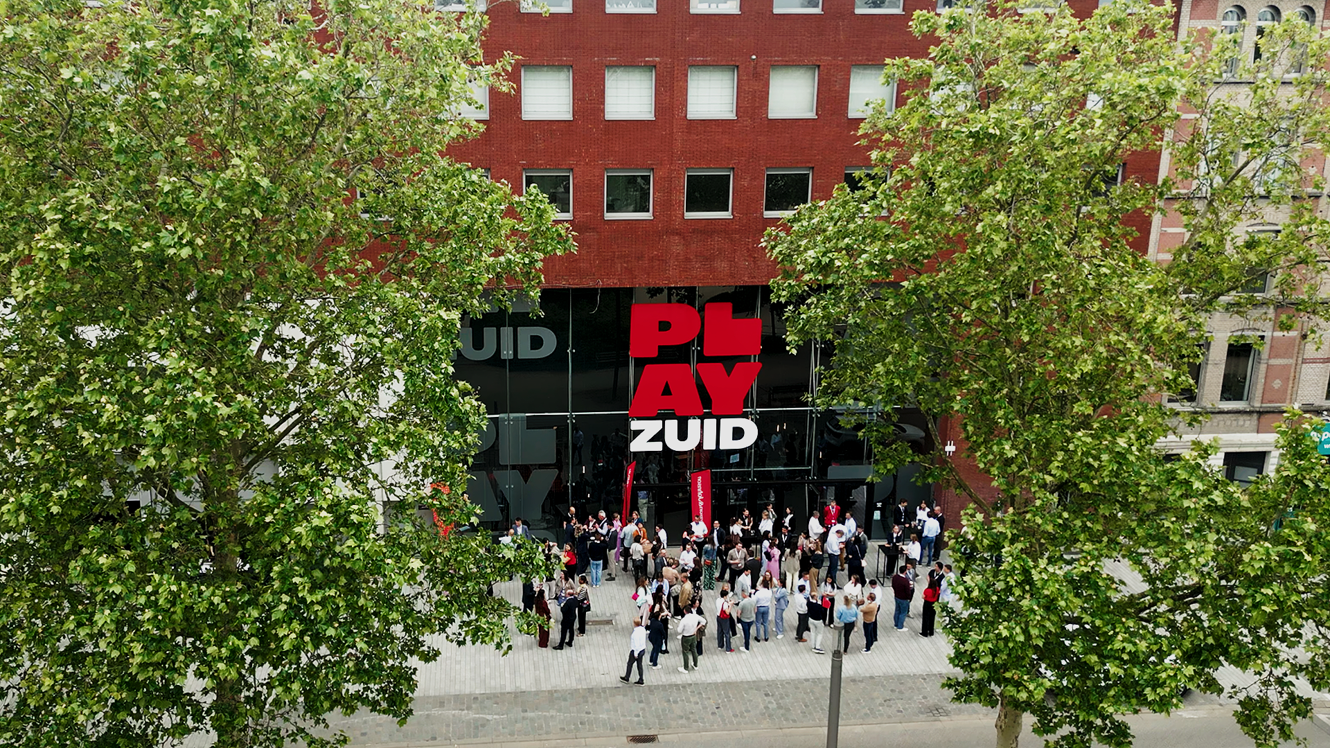 A large crowd gathered outside a building with the Play ZUID sign, surrounded by green trees. johnson & Johnson Finance day 2026 at Tv studio Play Antwerp Zuid