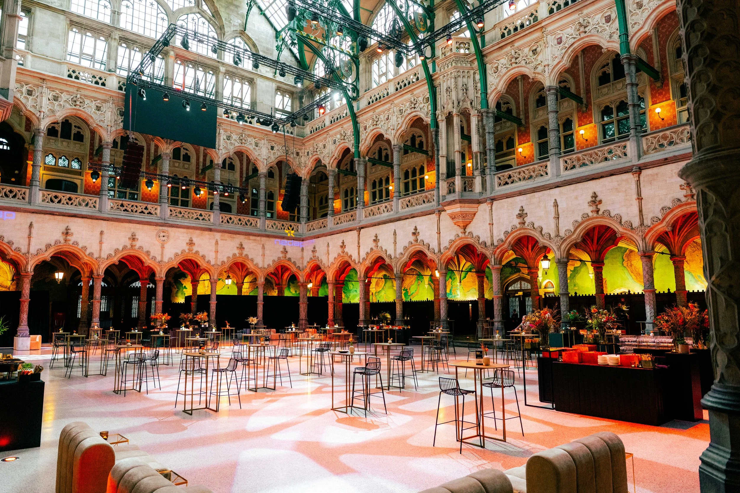 A large indoor event space with high arched windows, ornate architectural details, and a stage with lighting equipment.