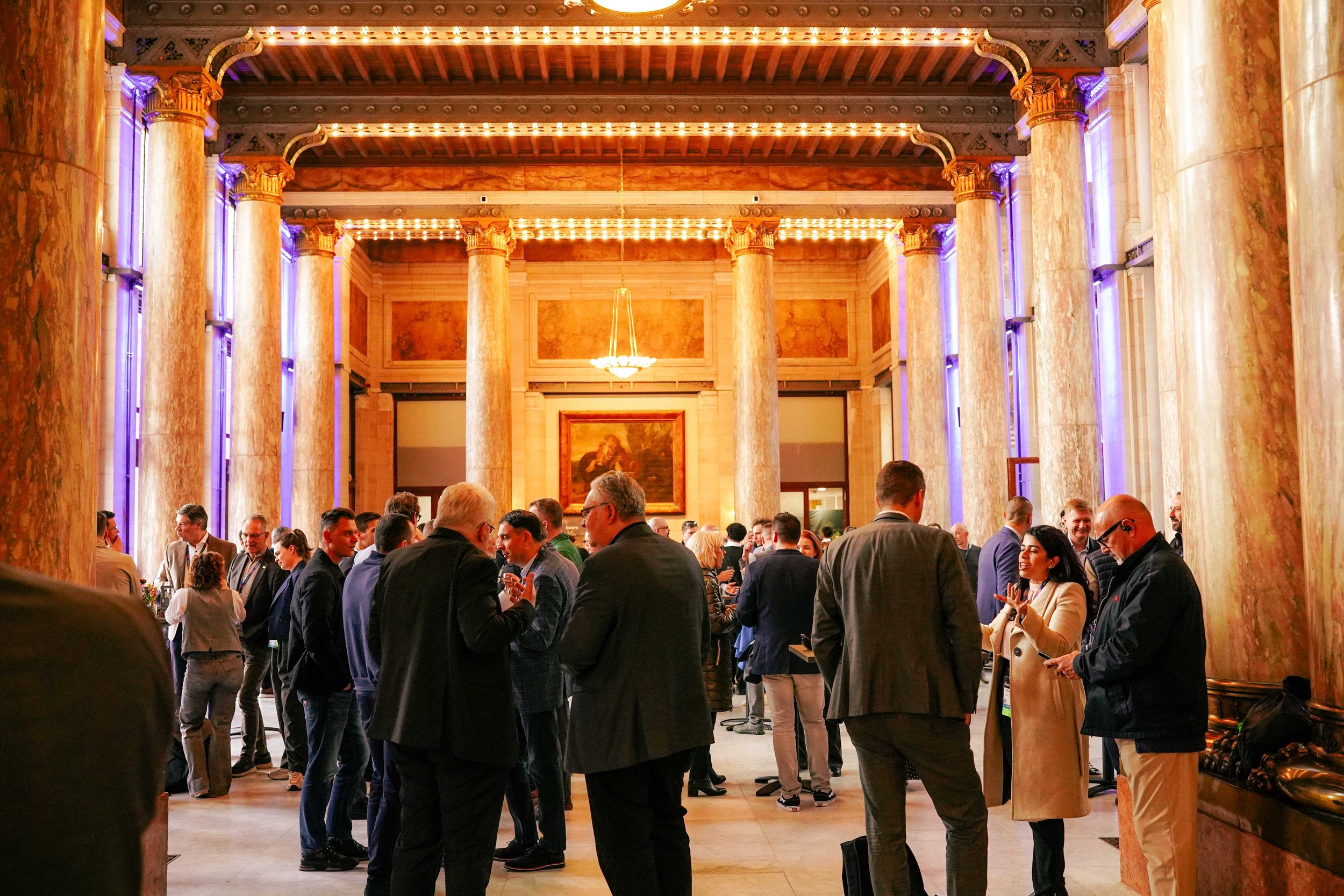 A large group of people dressed in formal and business attire gathered in an elegant, historical ballroom with tall marble columns, ornate ceiling, and warm lighting.ASIS EUROPE ANTWERP 2026 at the ZOO