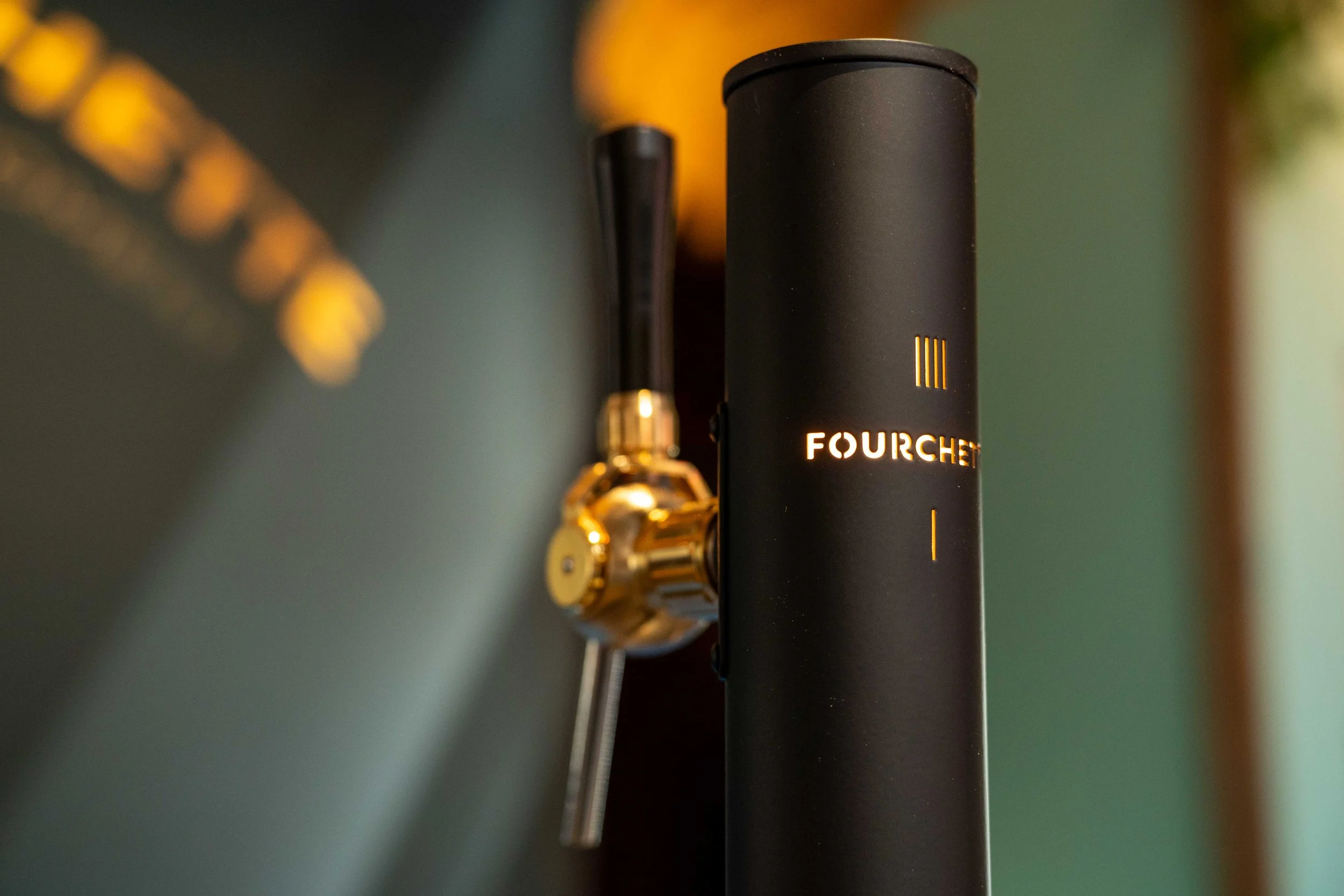 Close-up of a black device labeled 'FOURCHE' with a small yellow light, connected to a gold-colored connector on a metallic surface. Michelin guide Ceremony 2026 Antwerp, Handelsbeurs.
