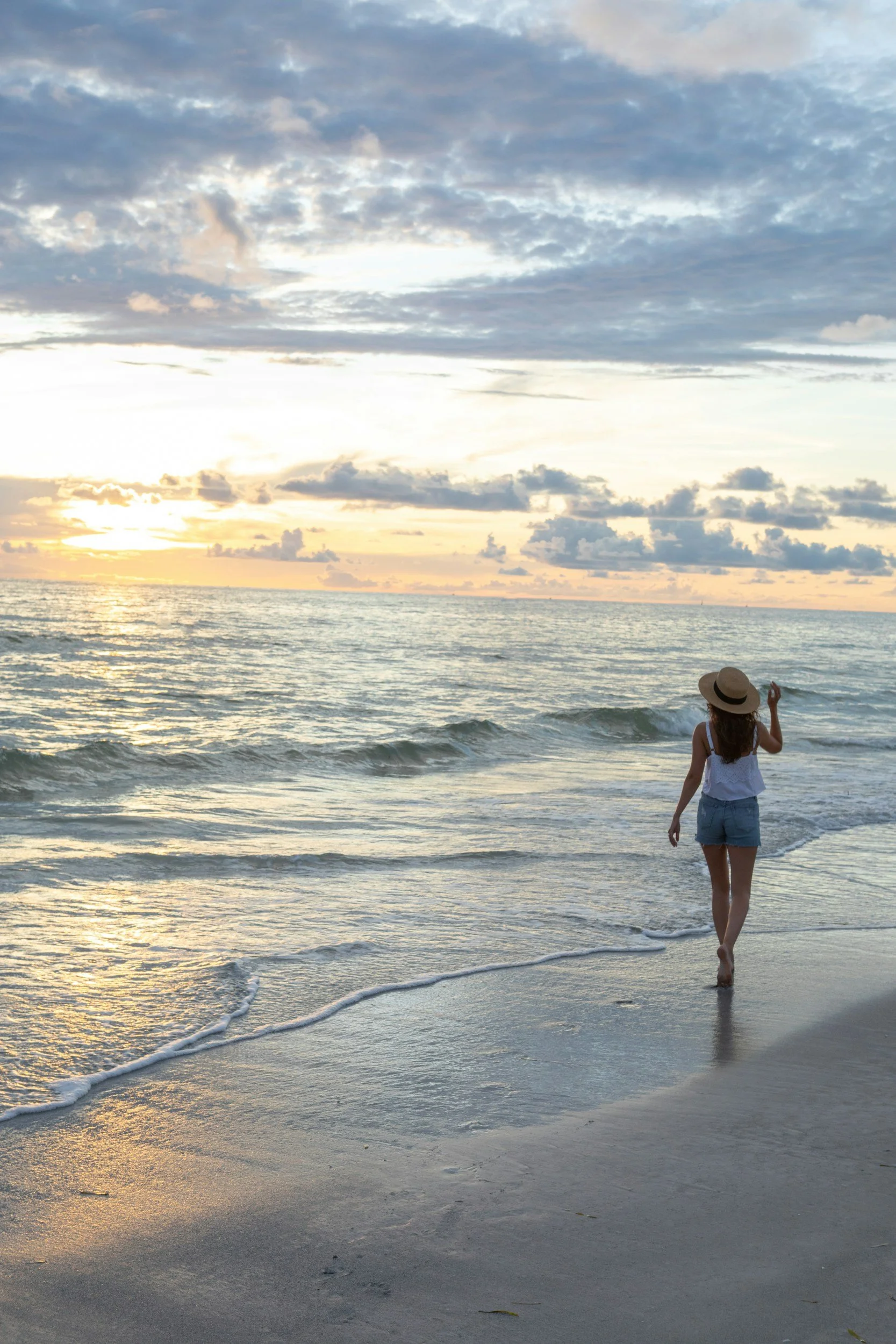 Woman walking along the beach at sunset, representing an individual journey of growth, reflection and transformation.