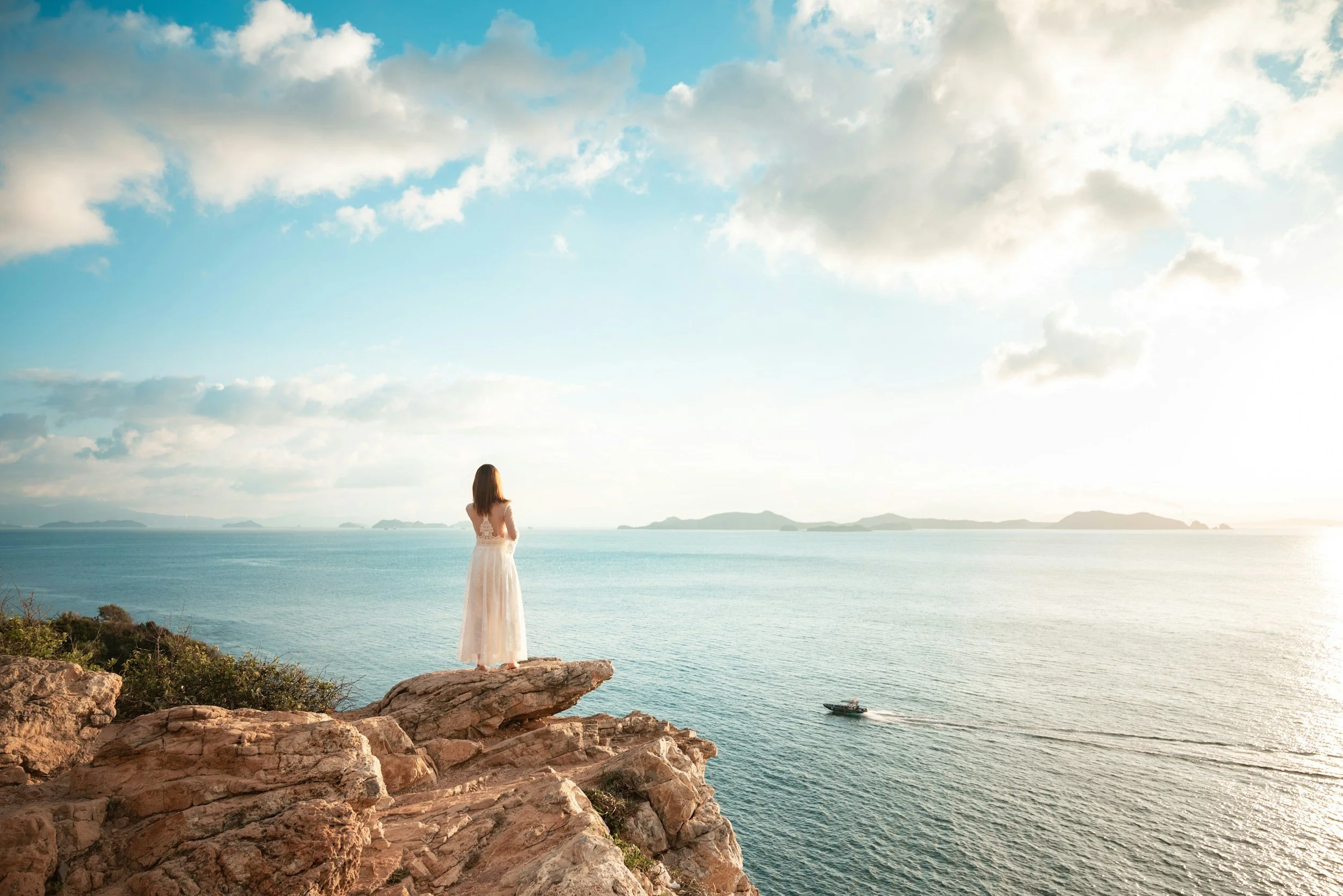 Woman standing on a rocky cliff looking out to sea, representing confidence, reflection and embracing a new chapter.