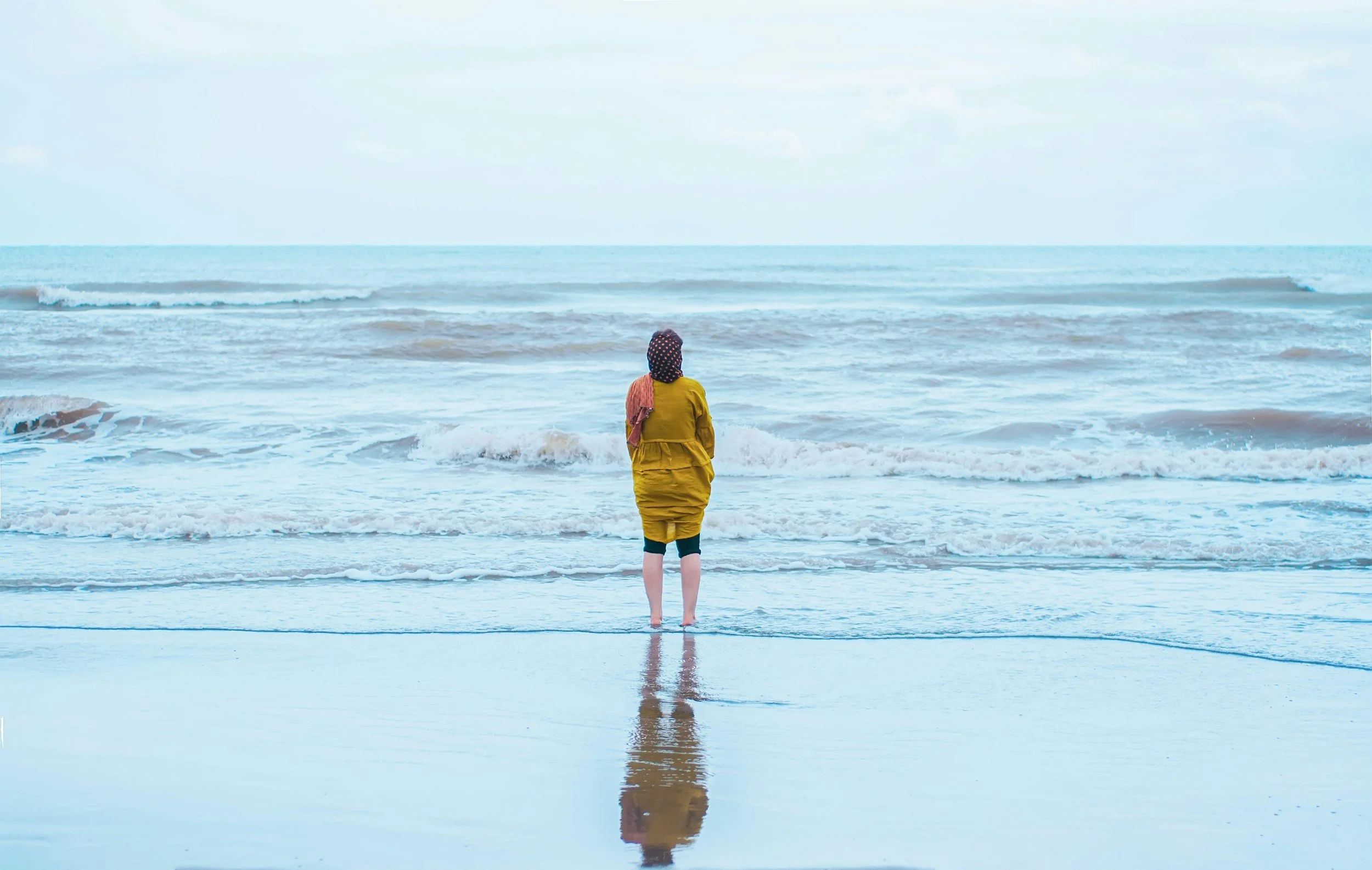 Woman standing by the sea with her shadow behind her during a reflective moment
