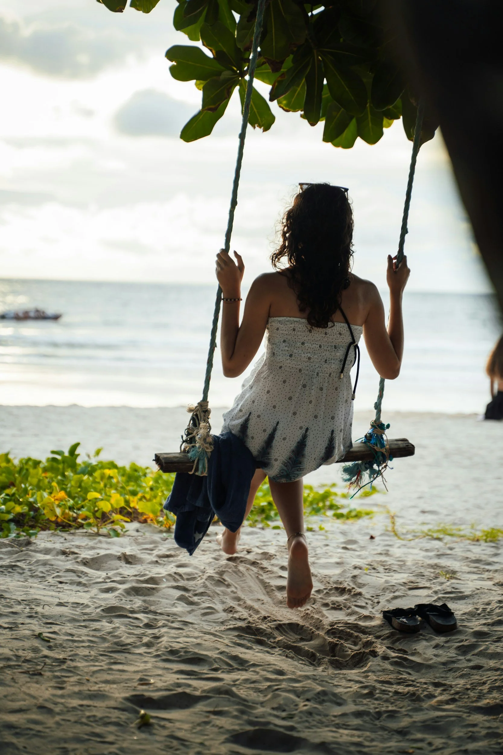 Woman sitting on a swing by the sea, representing a moment of pause, reflection and reconnecting with yourself.