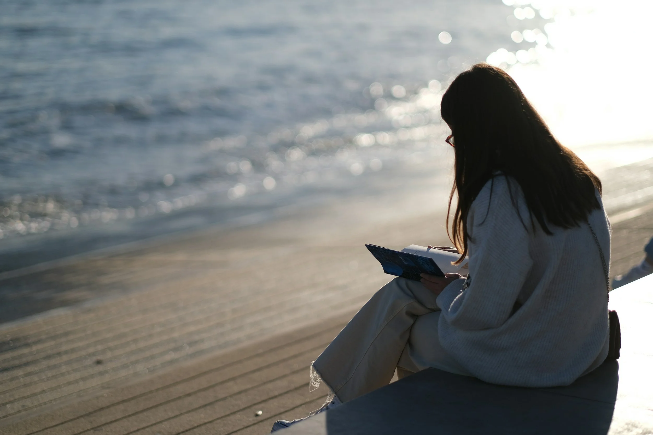 Woman sitting on the beach, quietly reading.