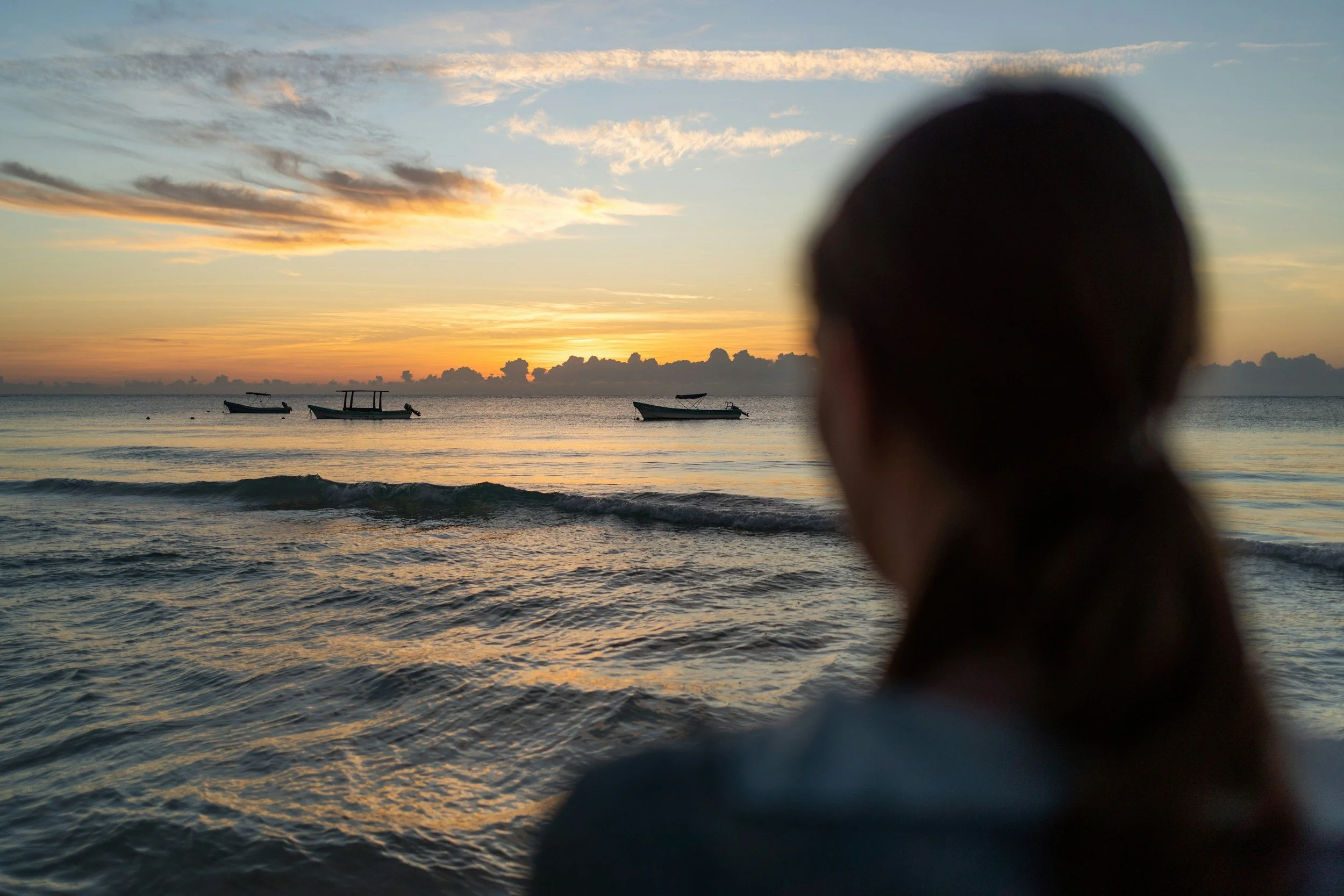 Person standing beside the sea at sunset, looking out across the water