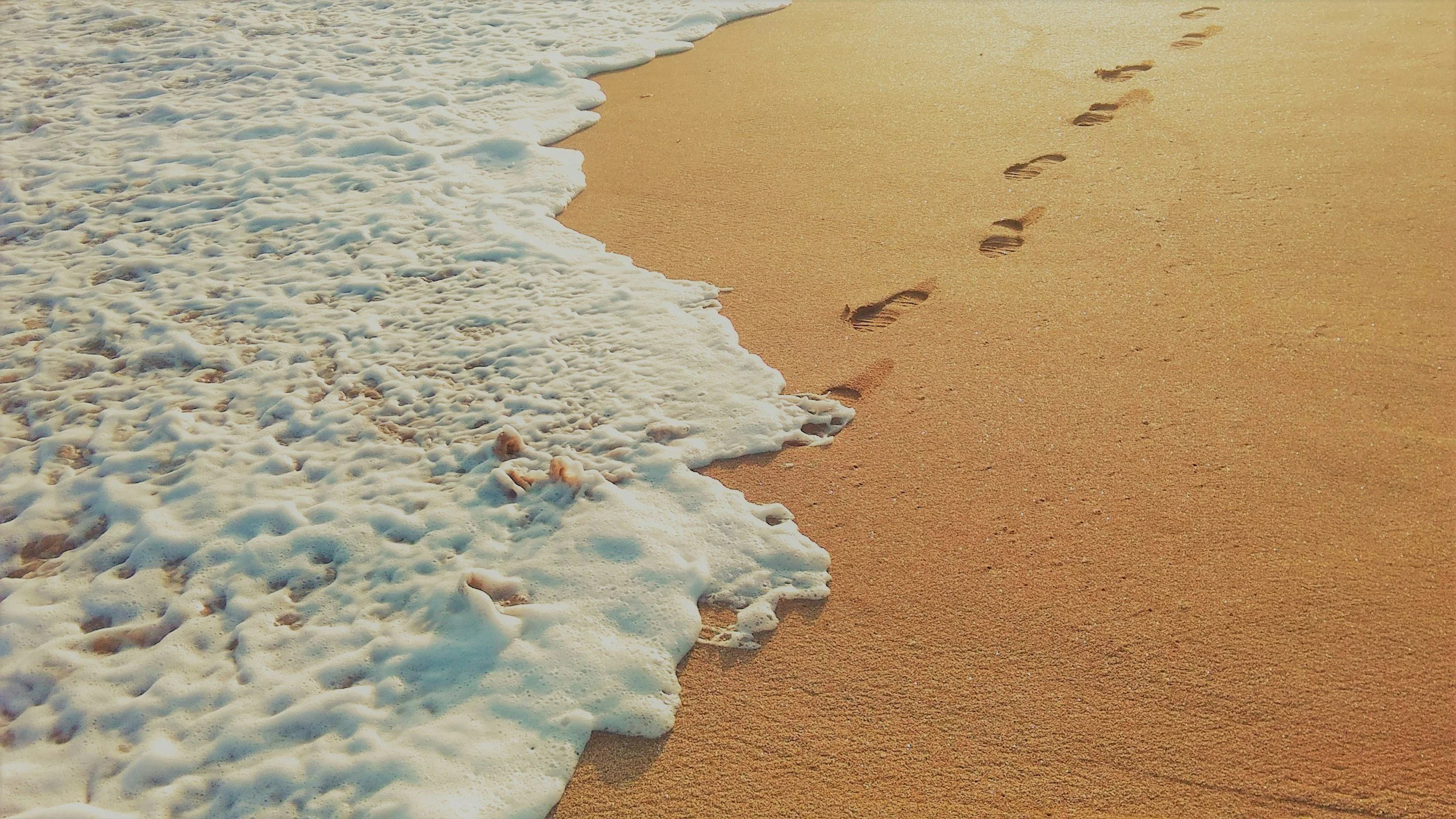 Footprints stretching across wet sand beside the sea.Footprints in the sand on a beach with gentle waves washing ashore.
