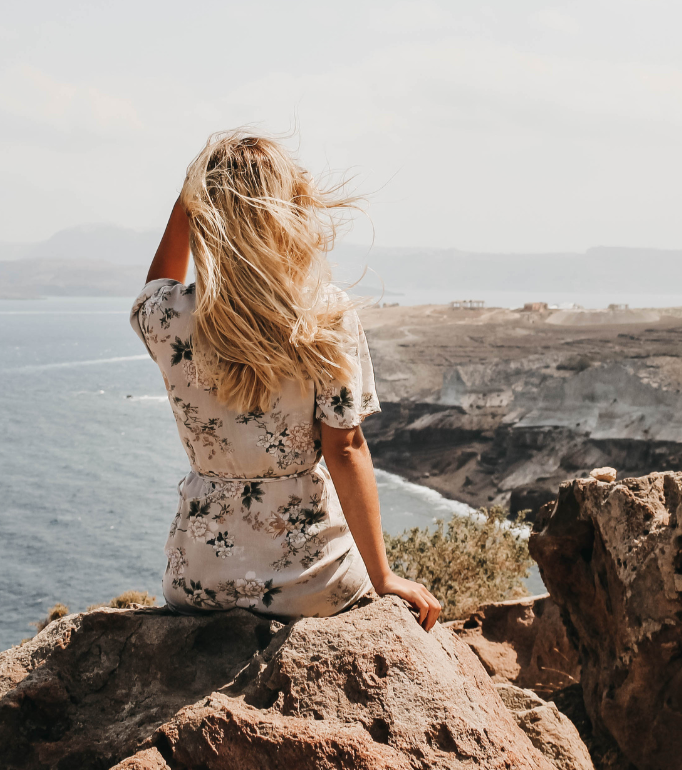 Woman sitting on rocks overlooking the sea and distant coastline.