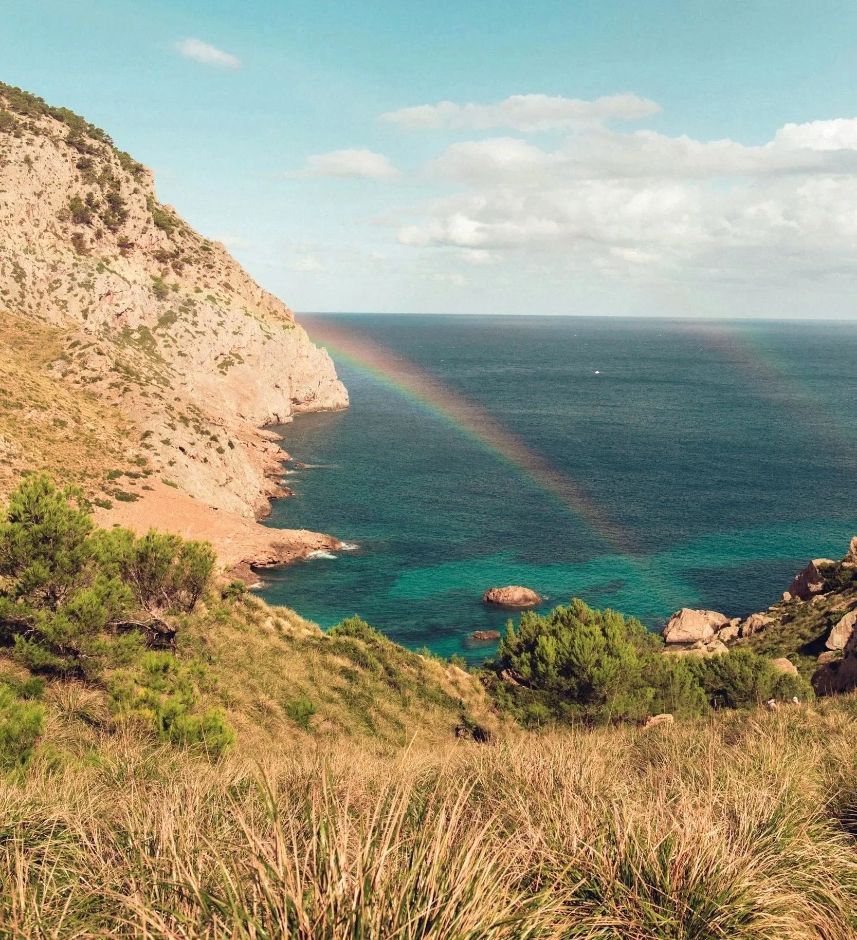 ocky cliffs overlooking a bright ocean with a rainbow, representing hope, connection and new possibilities.