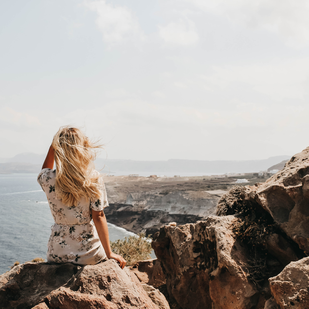 Woman sitting on coastal rocks overlooking the sea, symbolising the unique, personalised journey and meaningful transformation behind every Back to You™ experience.