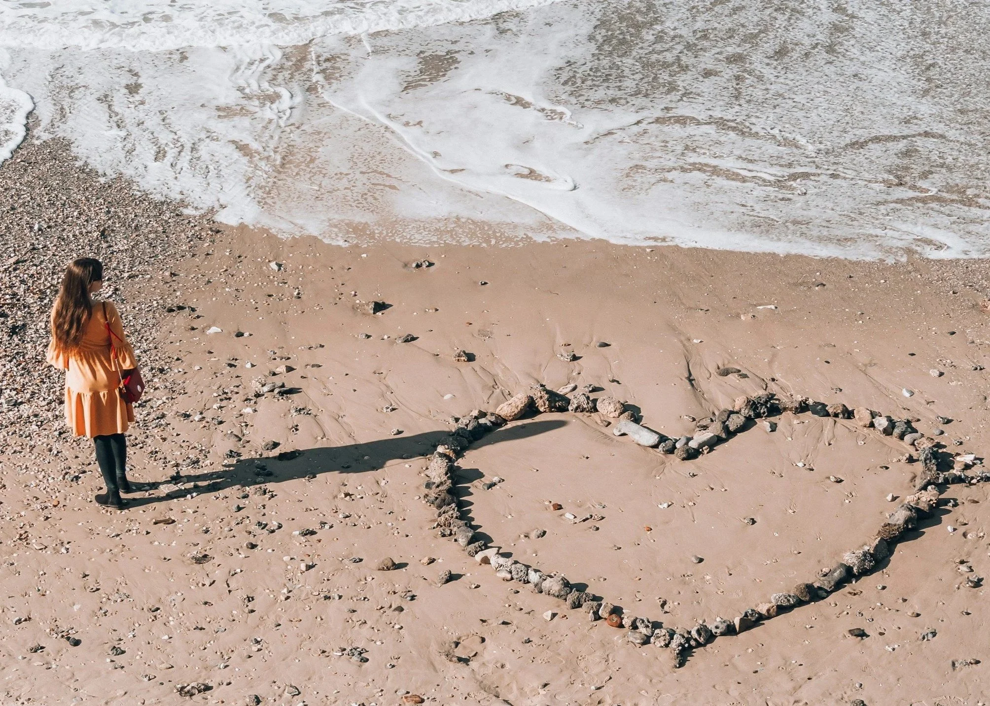 Woman standing on the beach beside a heart shape made from stones