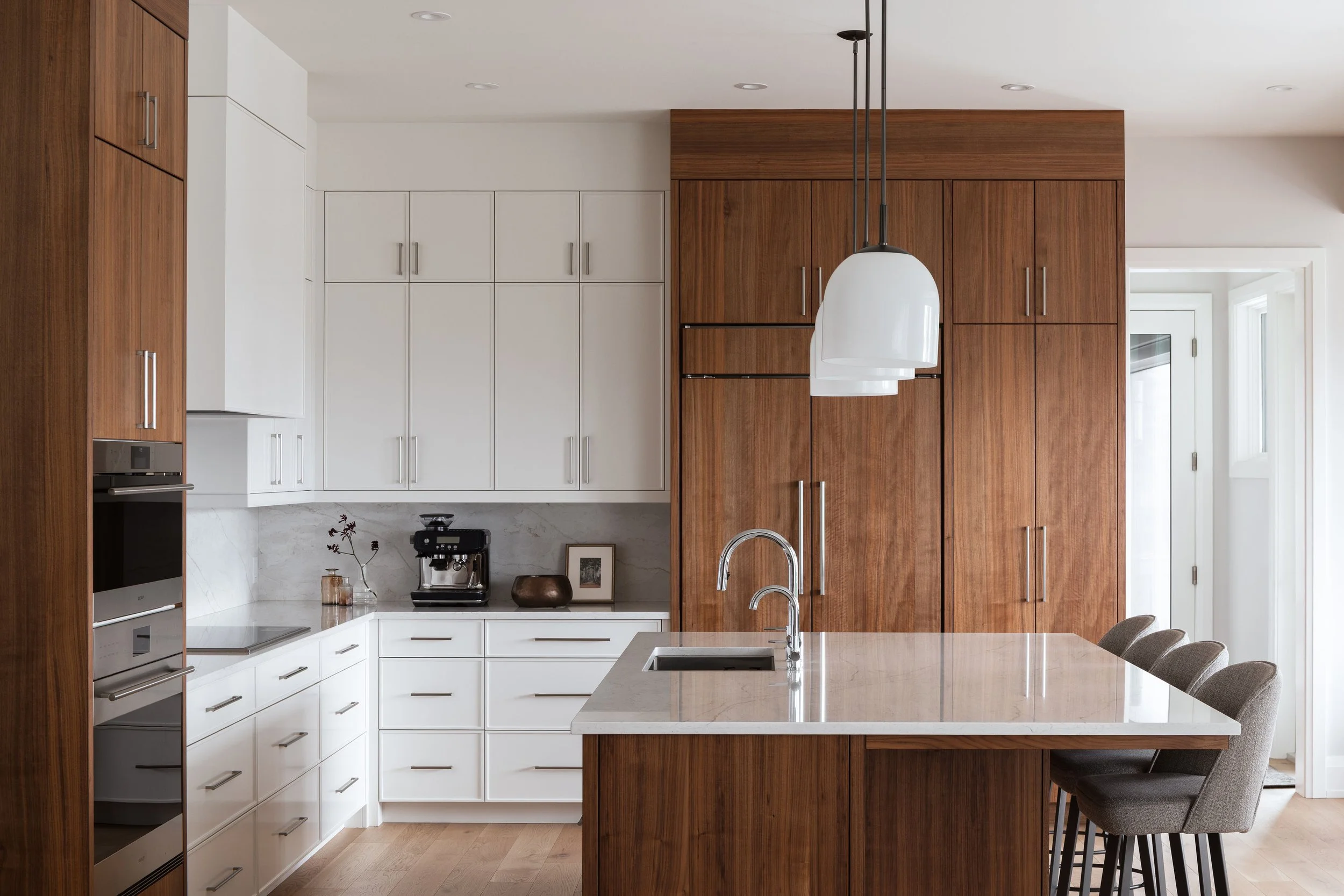 Custom Calgary kitchen featuring full-height walnut cabinetry, white millwork, integrated appliances, a large stone island and streamlined contemporary detailing by Dashney Interiors.