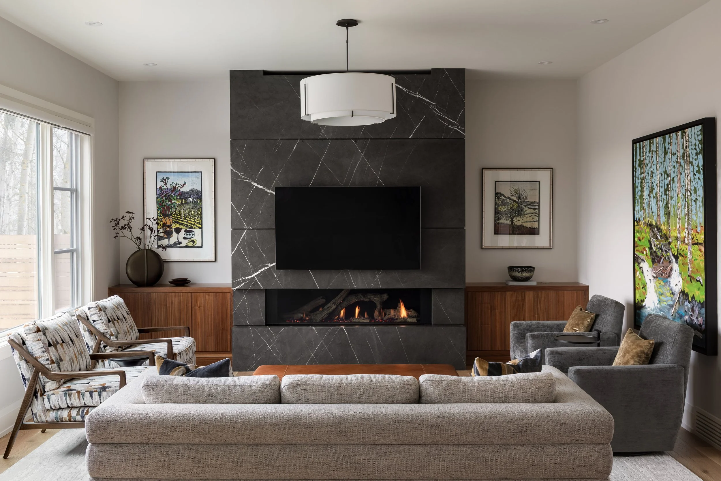 Contemporary Calgary living room by Dashney Interiors featuring a dramatic black stone fireplace, custom walnut built-ins, layered artwork, upholstered seating and warm natural finishes.