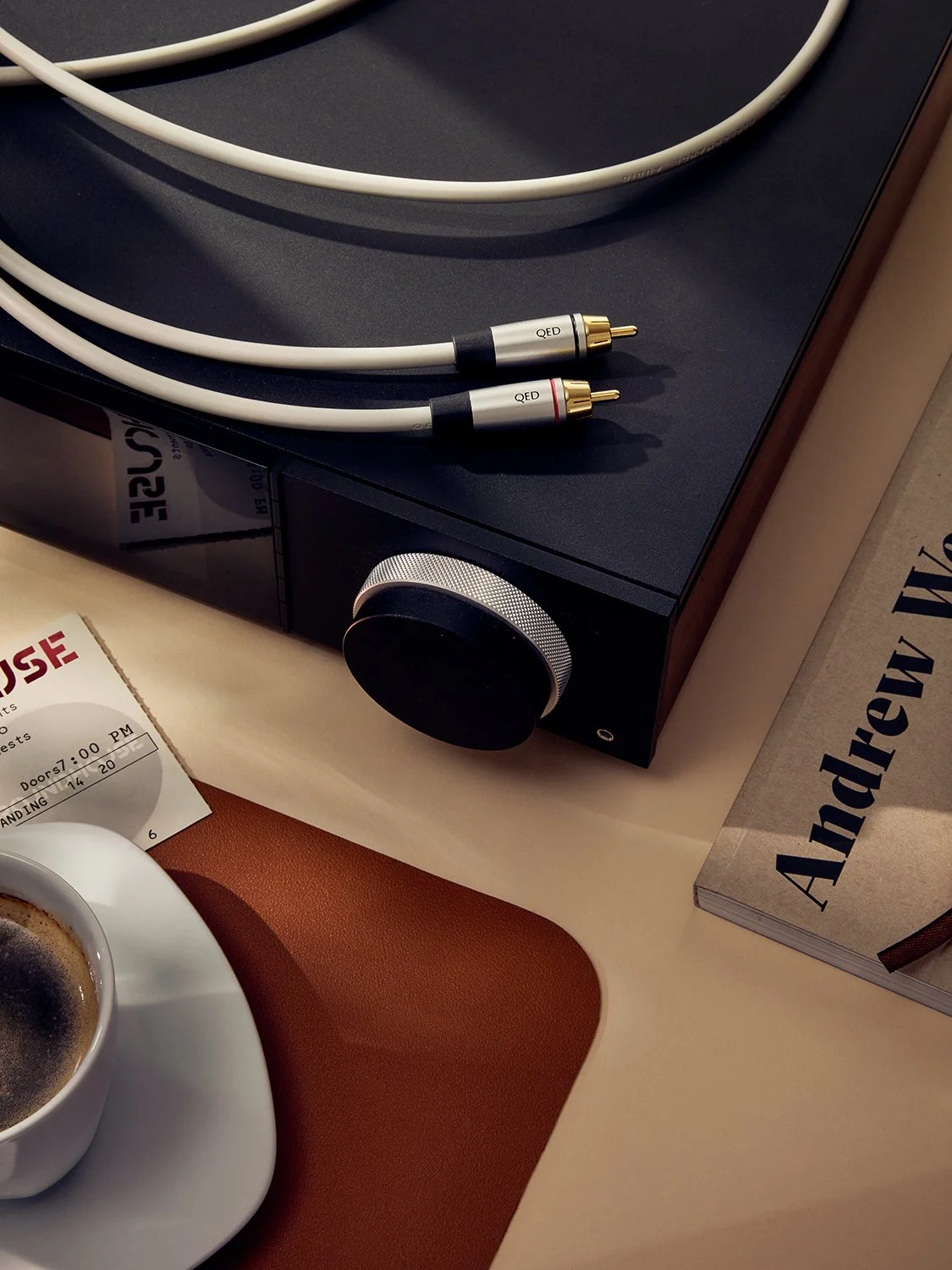 Turntable with white audio cables, a cup of coffee, a concert ticket, and a book titled 'André V' on a table.