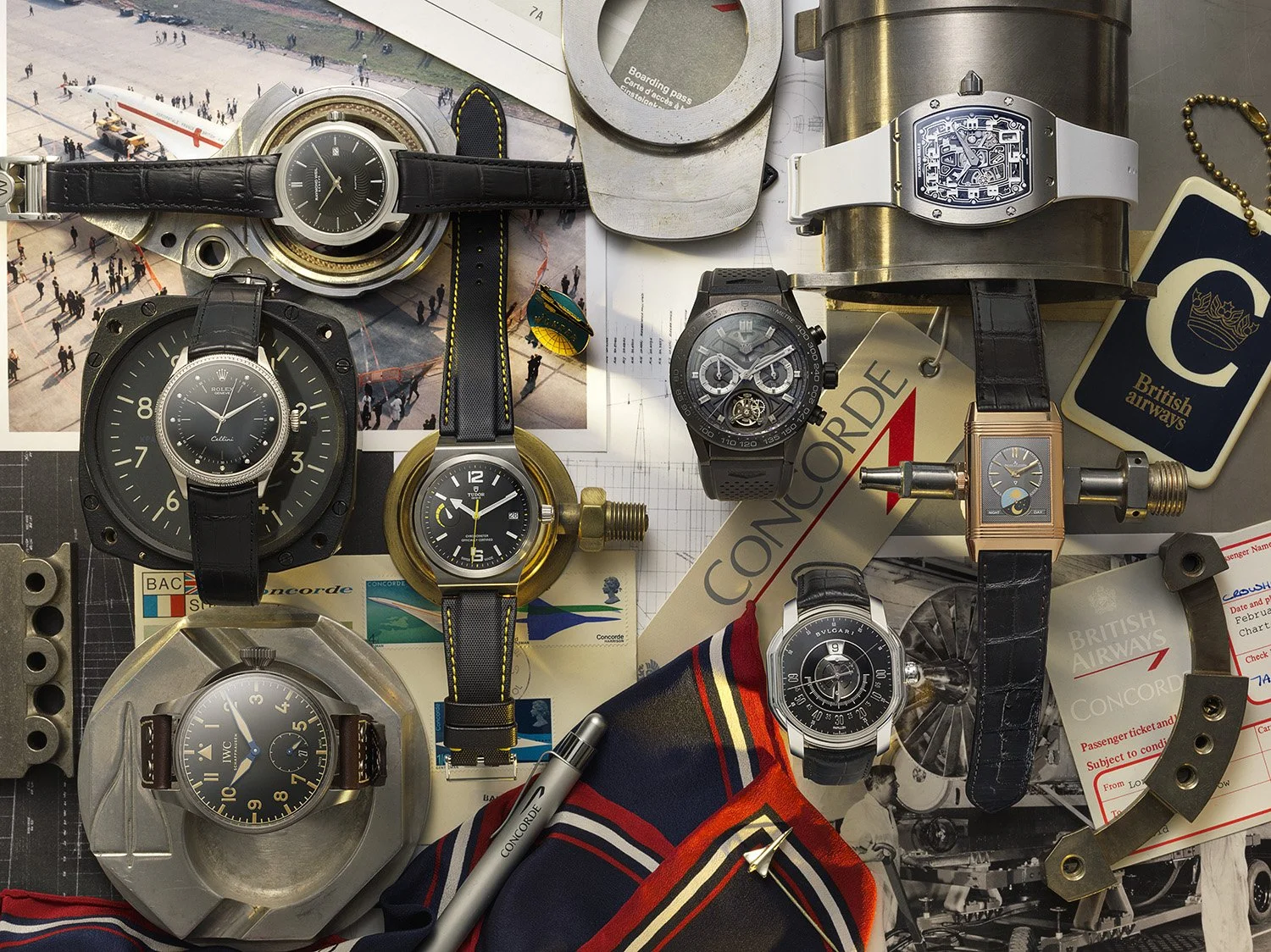 A flat lay of various wristwatches, airline tags, a Concorde branded pen, and miscellaneous travel-related items on a surface.