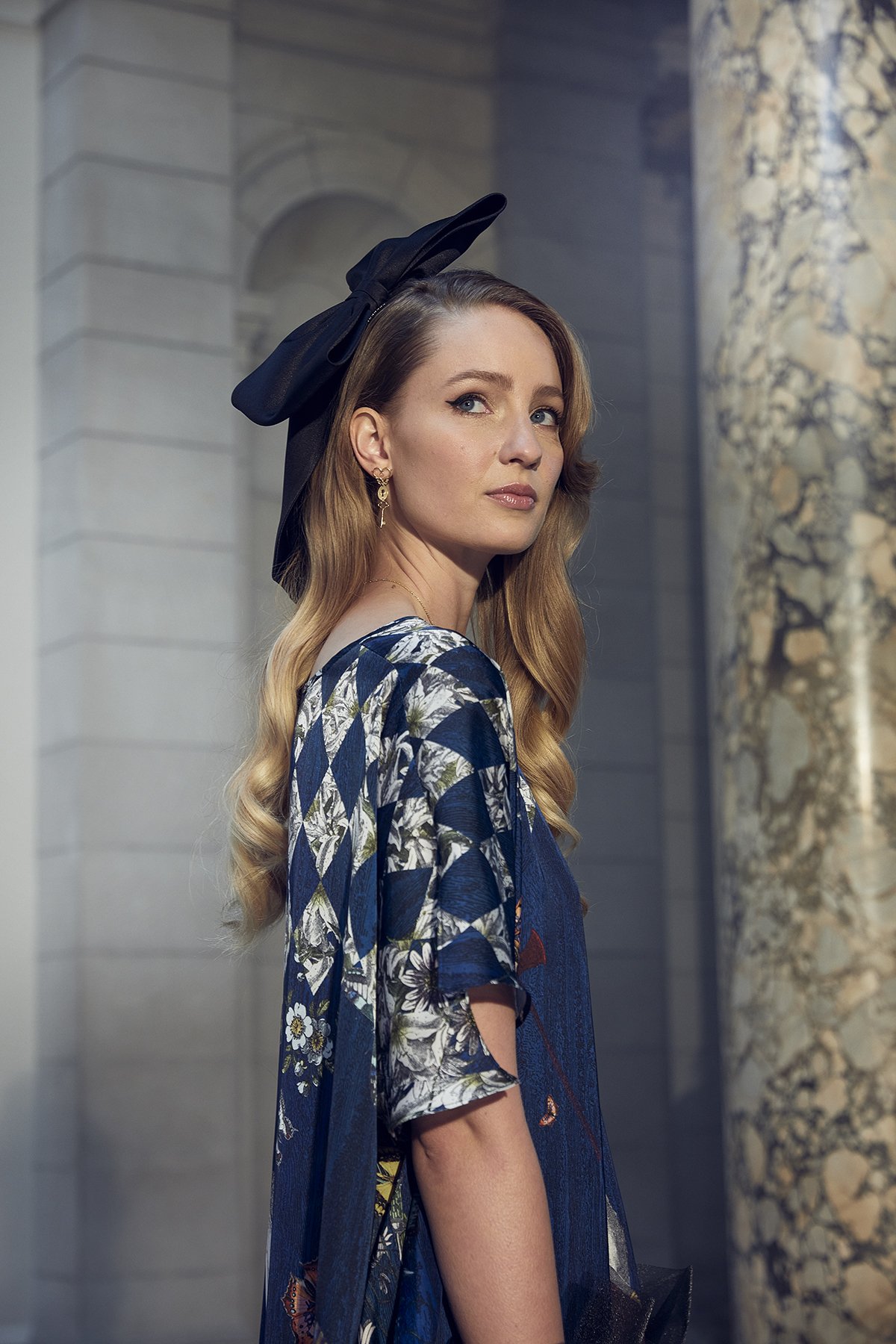 Woman with long blond hair wearing floral patterned dress and black bow in elegant setting