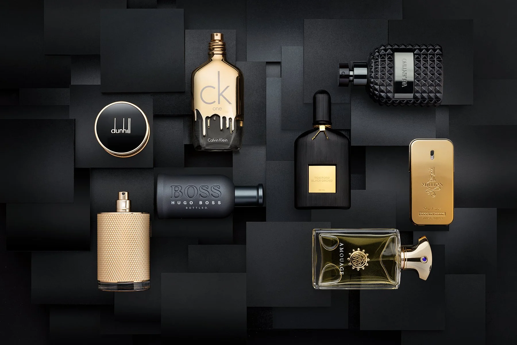 A flat lay of various luxury perfume bottles and a compact, arranged on a black geometric background.