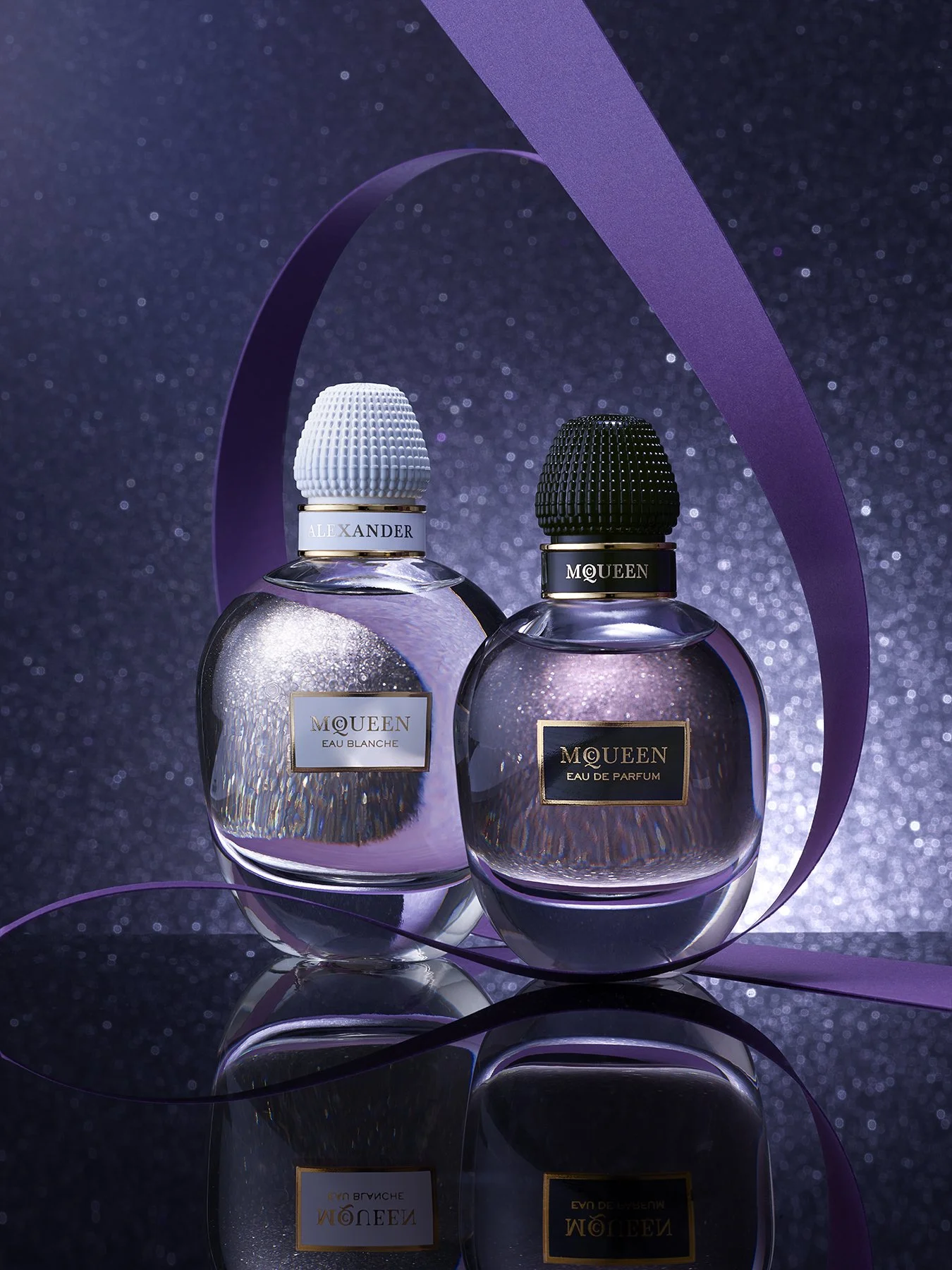 Two perfume bottles from McQueen, one labeled Eau Blanche and the other Eau de Parfum, against a glittery background with purple ribbons.