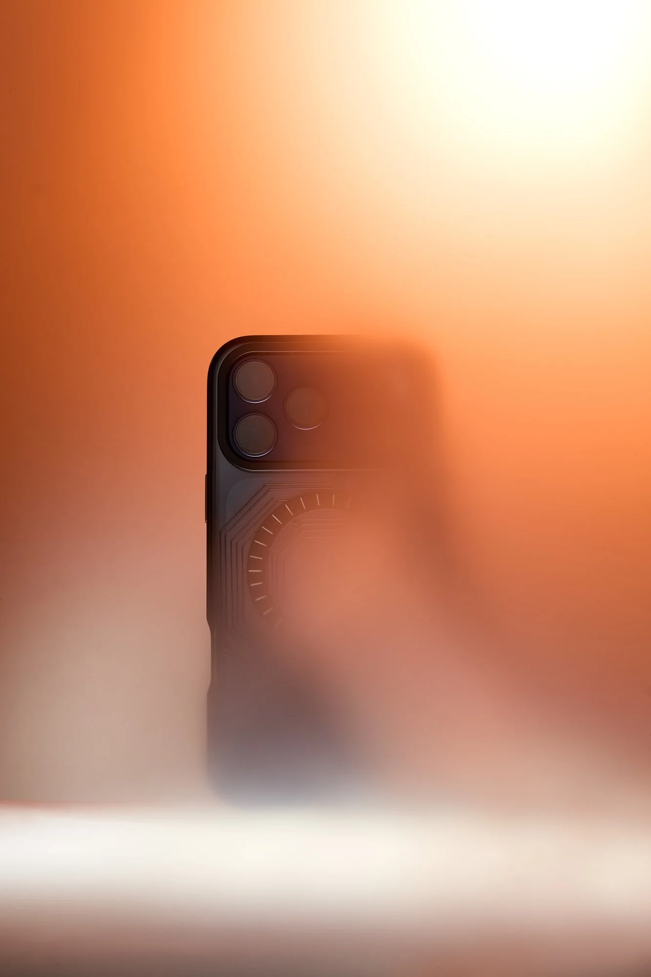 Close-up of the top part of a smartphone with a triple camera setup against a blurred orange and yellow background.