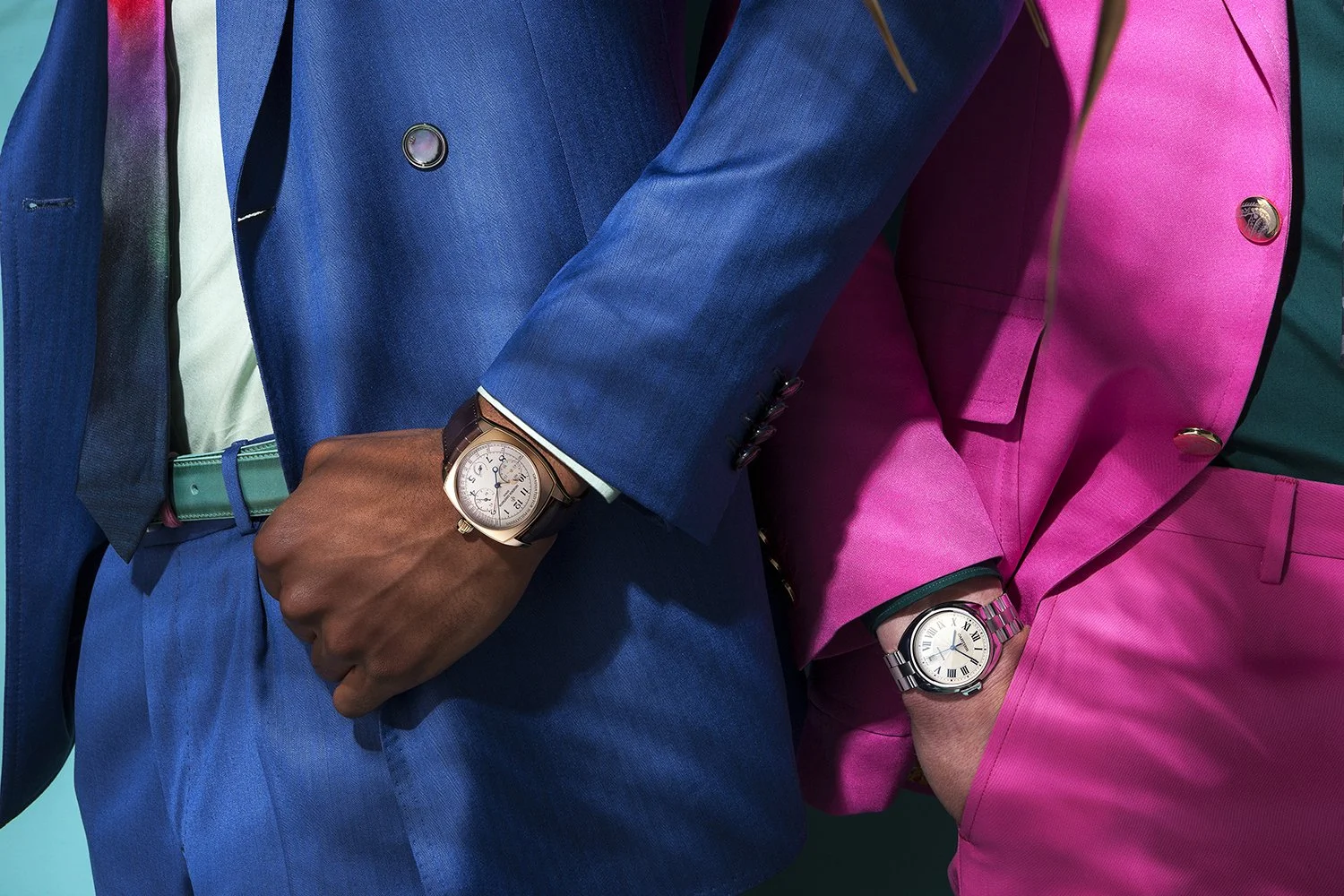 Close-up of two people wearing colorful suits, displaying watches on their wrists.