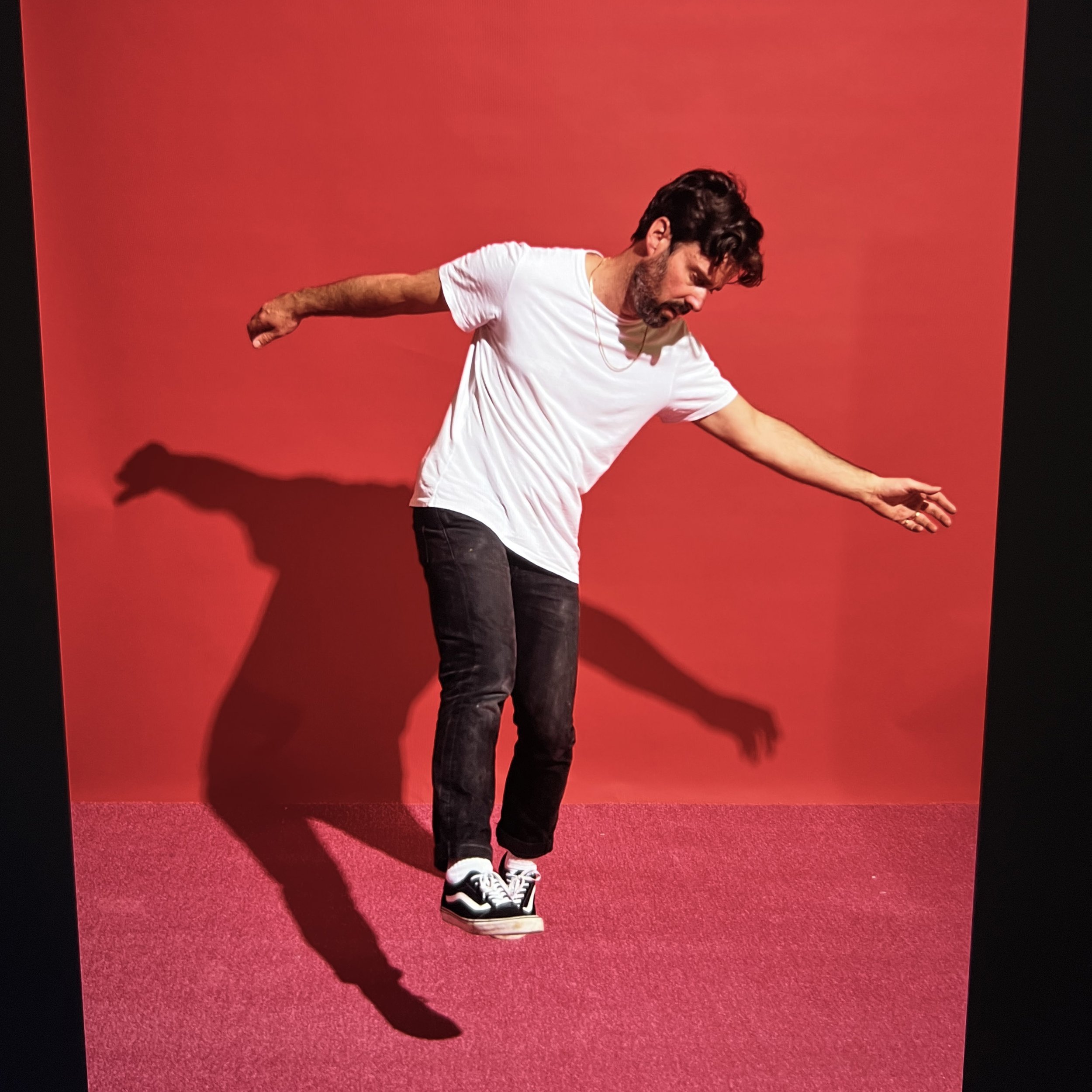 Man in casual clothing jumping in front of a red background, casting a shadow on the wall.
