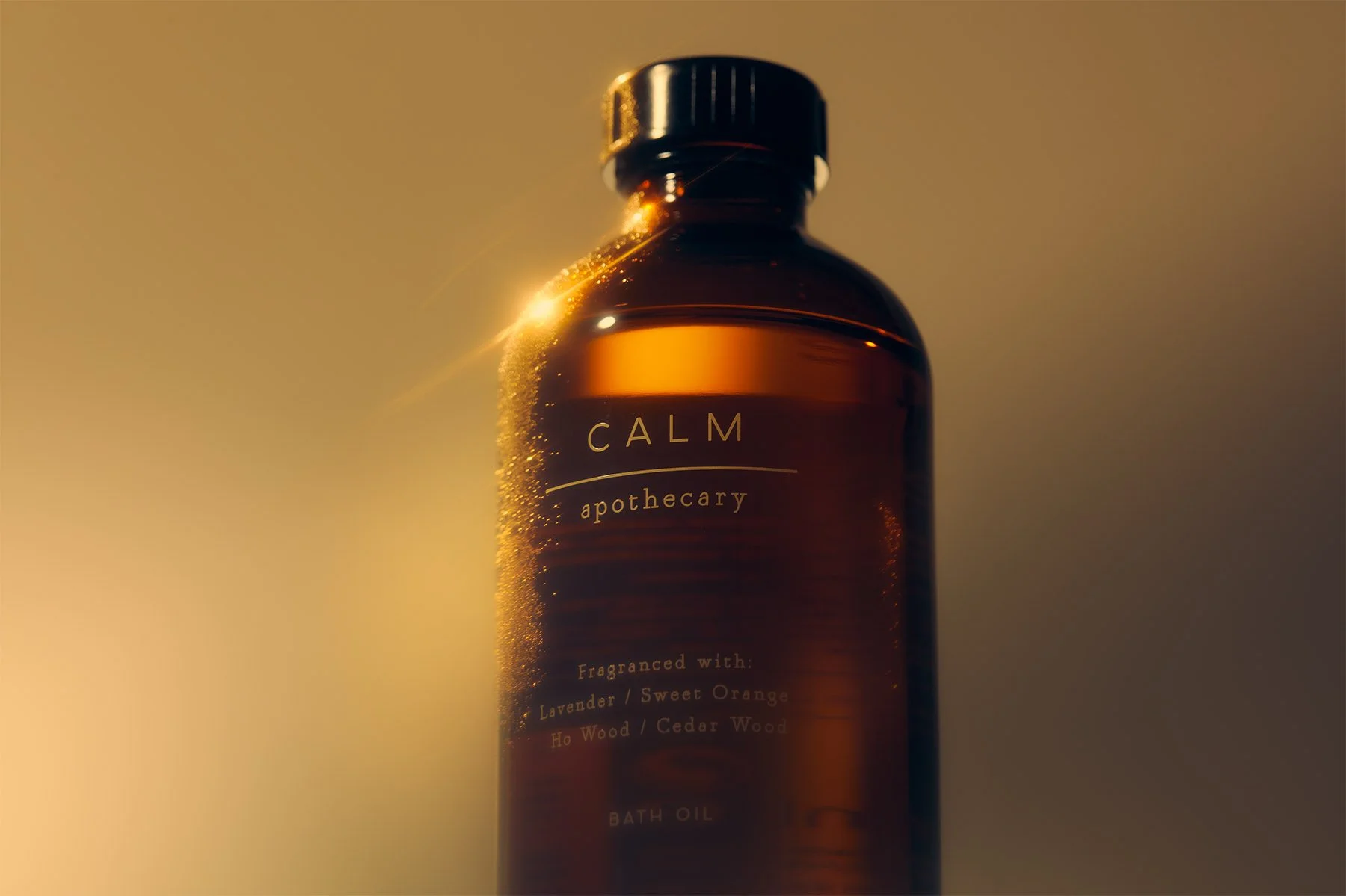 Amber glass bottle labeled 'CALM apothecary' with fragrance notes of lavender, sweet orange, and cedar wood, set against a warm, blurred background.