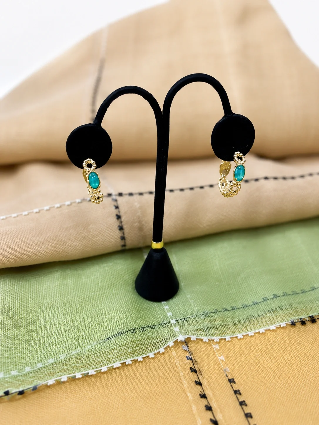 Pair of black earrings with gold and turquoise accents displayed on a black stand with multicolored cloth background.