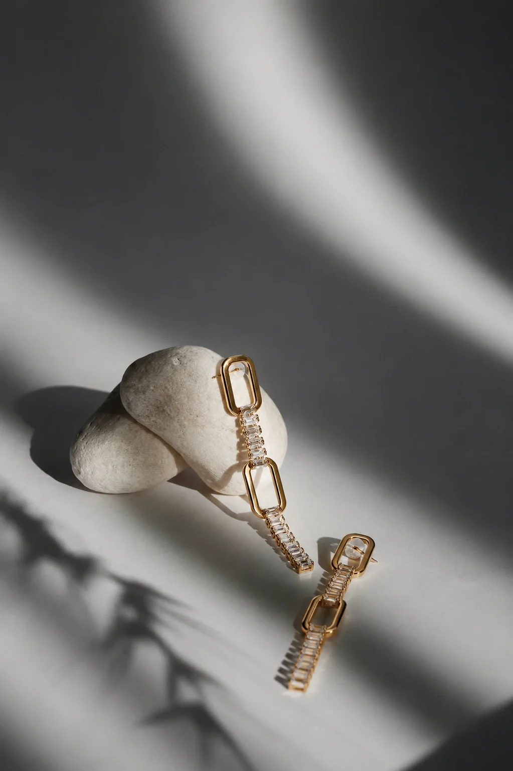 Gold and diamond link earrings placed on a white stone with shadowed background.