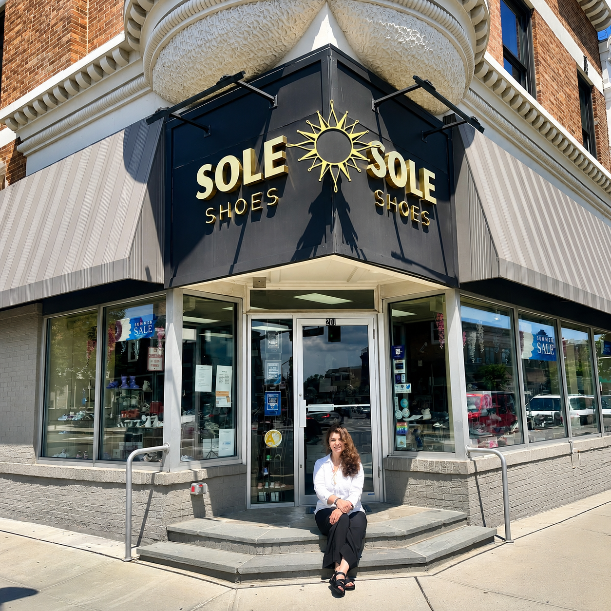 Woman sitting on steps in front of a shoe store in the Arcanum Hall building with the sign 'Sole Shoes' and a 'Summer Sale' window display.