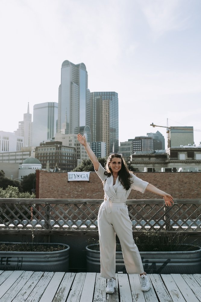 Christy stands on rooftop with skyline in background arms outstretched