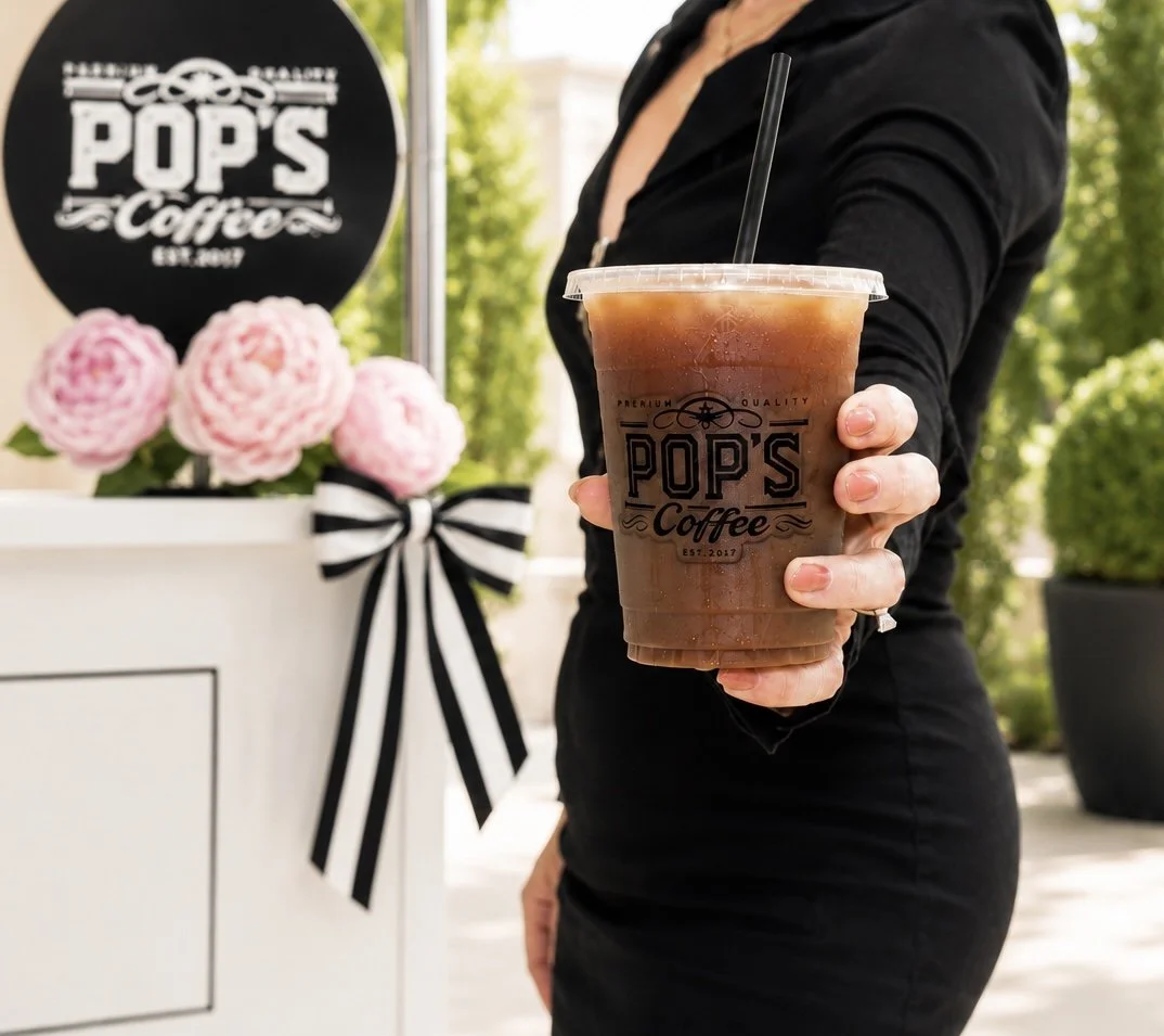 Hand holding signature food brew coffee in front of the Pop's Premium Coffee cart and floral styling.