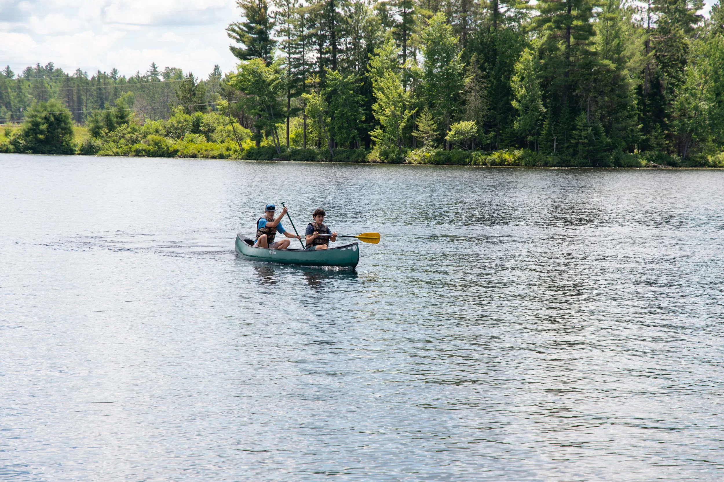 Two people in a green canoe on a lake with trees and a blue sky in the background.