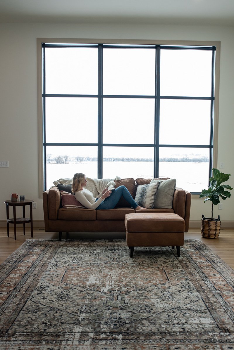 Whitney Bird Sitting reading on a couch in front of her window