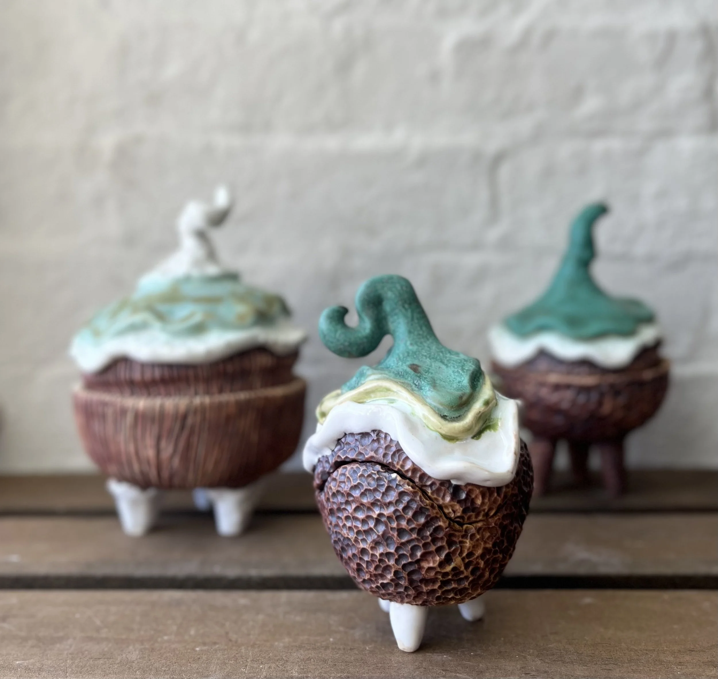 Three cupcakes with textured brown bases, white and green frosting, and green decorative toppers, displayed on a wooden surface against a light background.