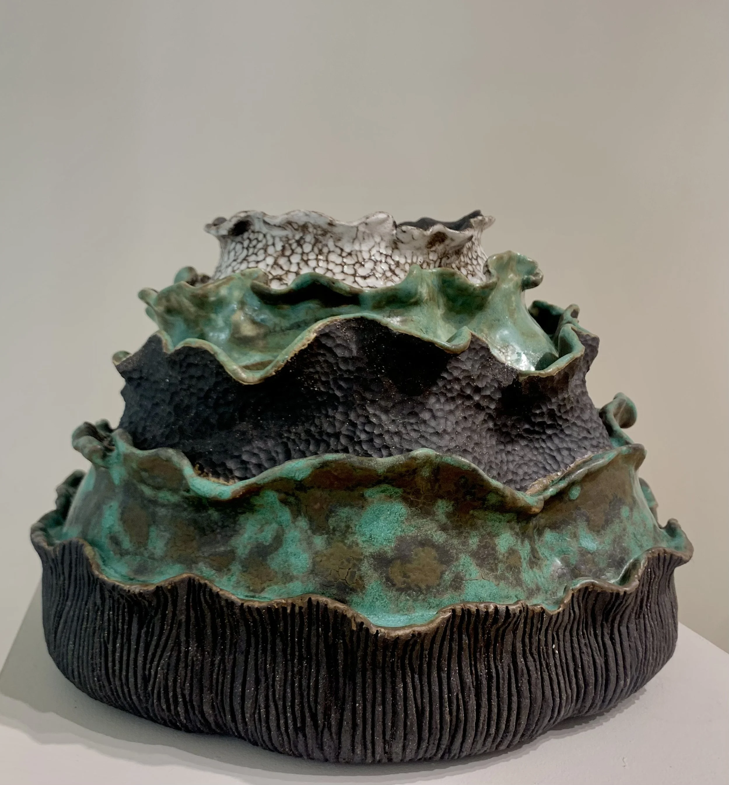 Multicolored, ruffled ceramic sculpture with textured, glazed surfaces in black, green, brown, and white