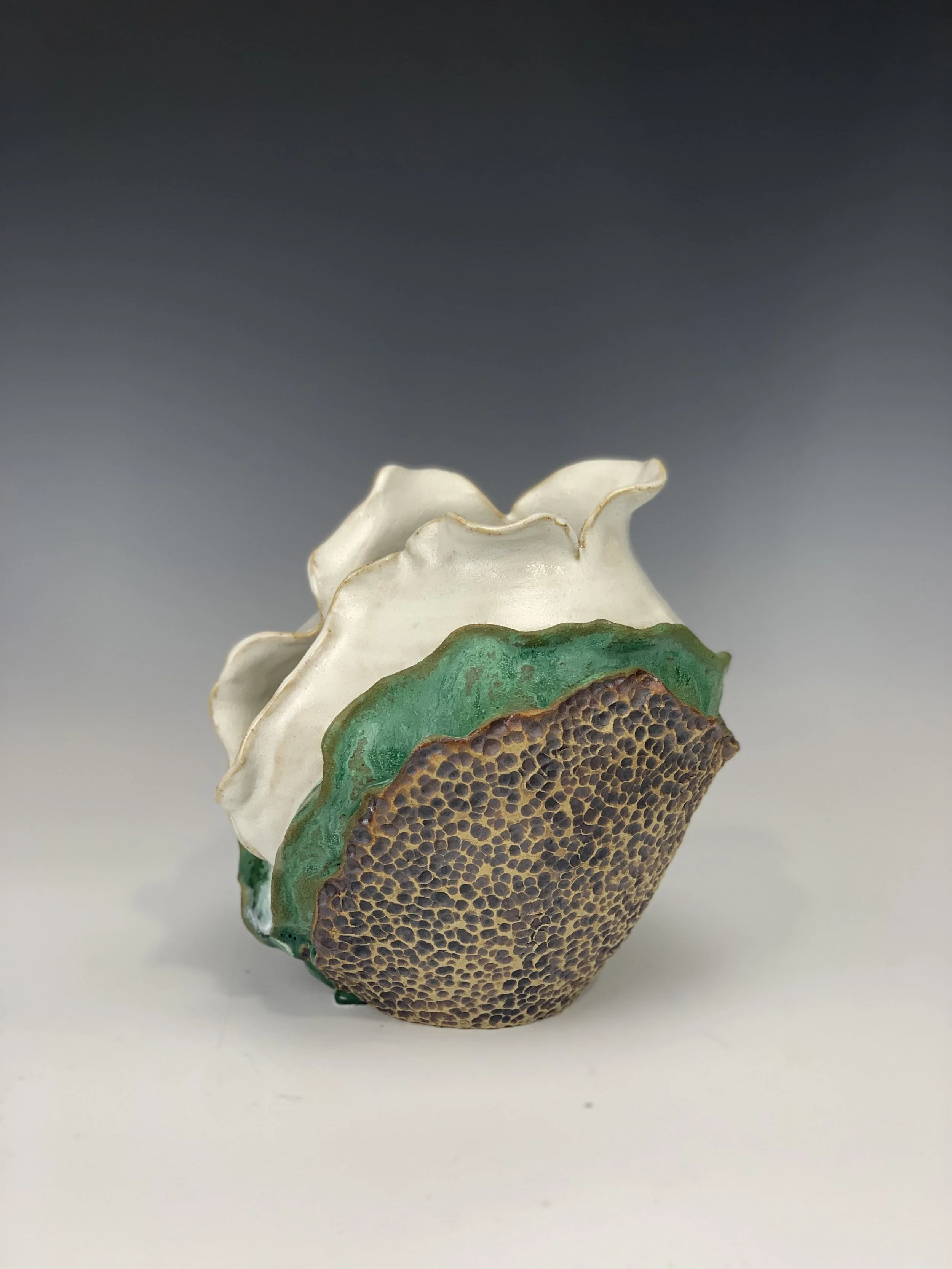 Ceramic art piece resembling a flower with a textured brown base, green accents, and white ruffled petals, set against a gradient gray background.