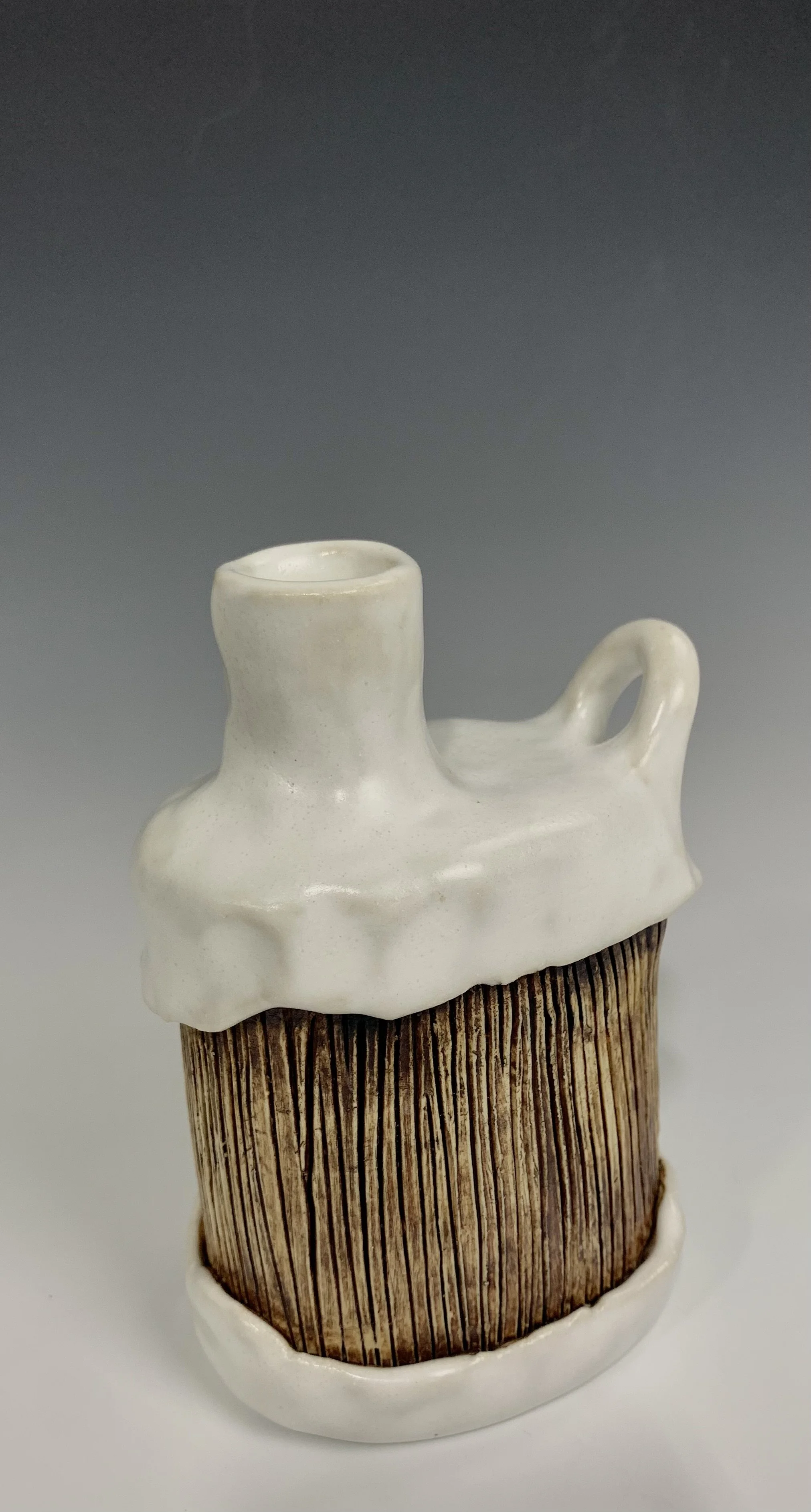 Ceramic vessel designed to look like a piece of wood with a white, melting roof and handle.