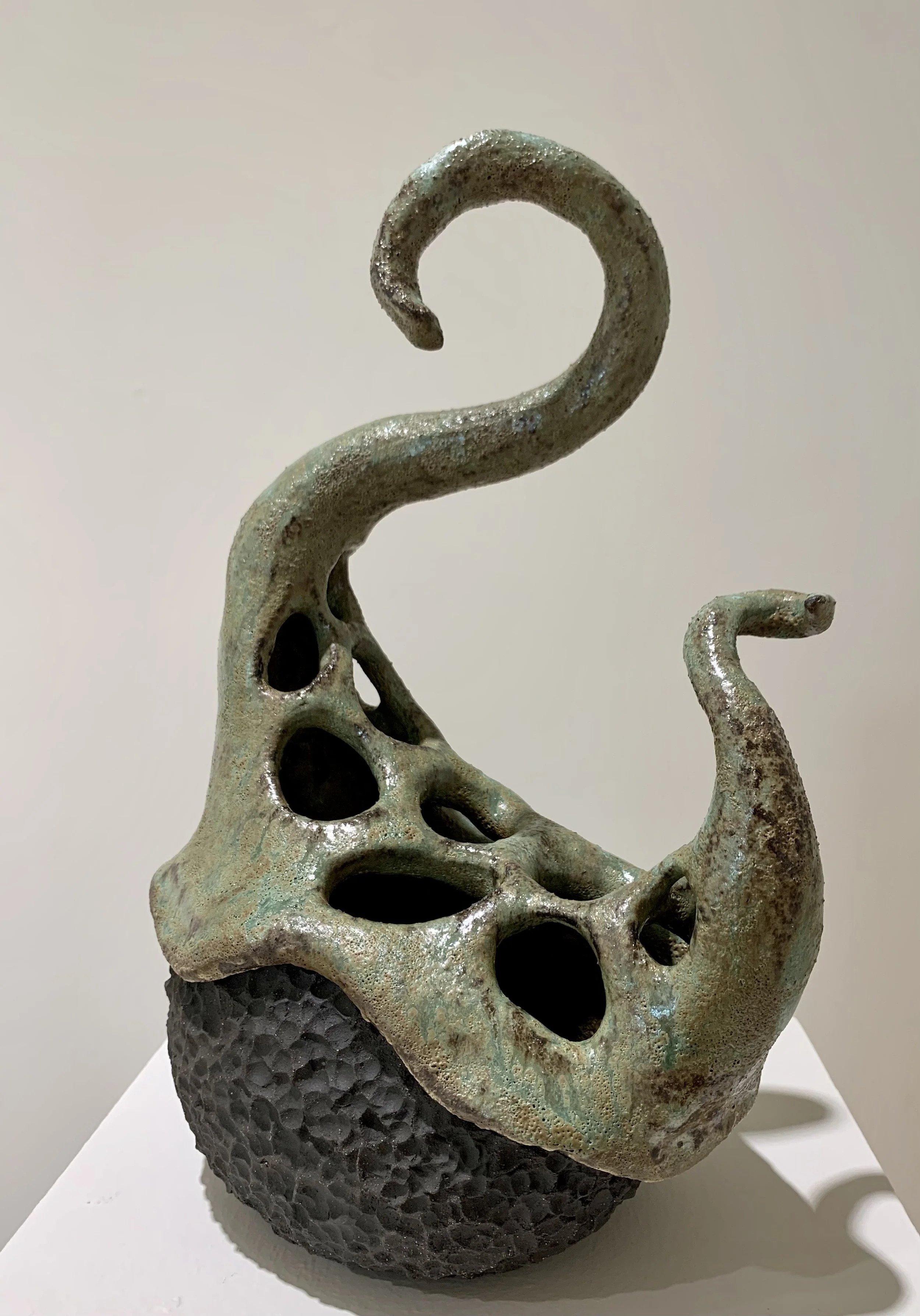 Ceramic sculpture featuring open holes and twisted, horn-like projections on textured black base.