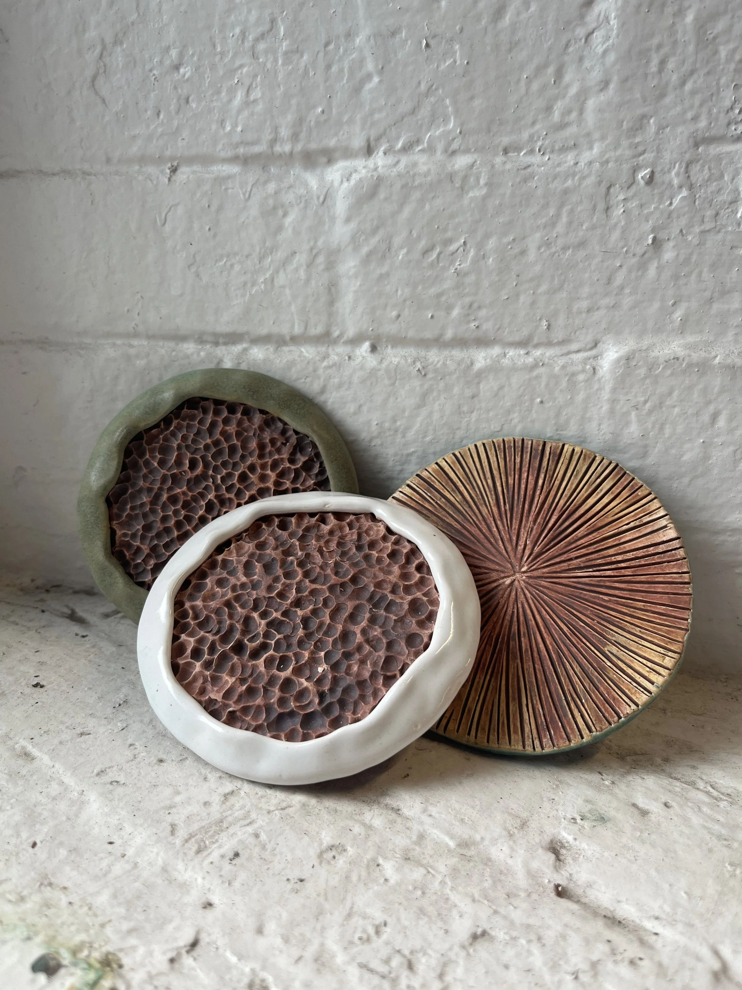 Three decorative ceramic dishes with textured patterns, placed on a concrete surface against a white brick wall.