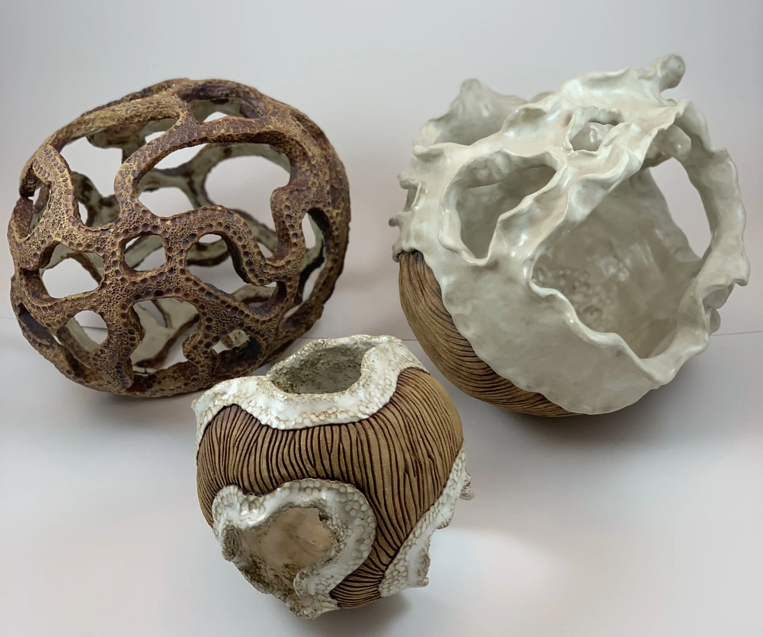 Three decorative ceramic vessels with organic, openwork designs and textures, arranged on a white surface.