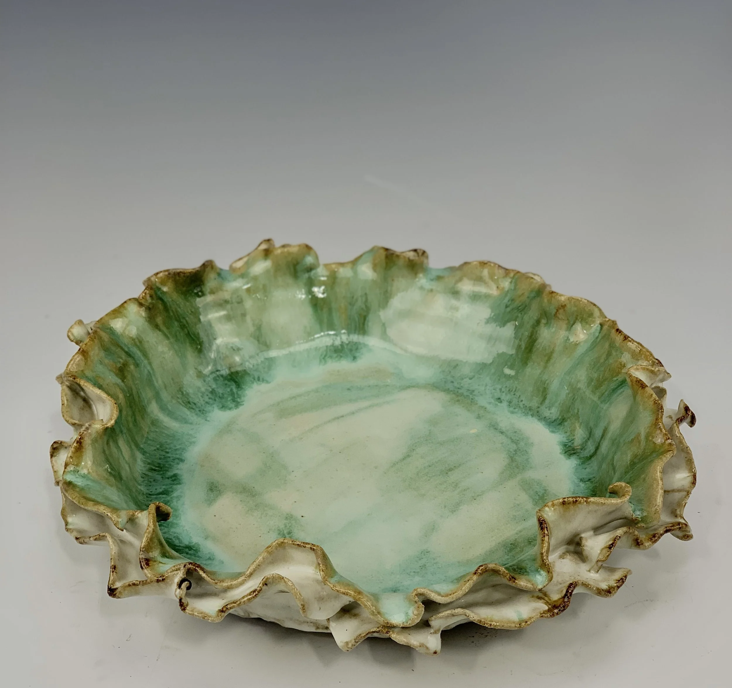 A ceramic bowl with ruffled, uneven edges and a glazed interior in shades of green and white.